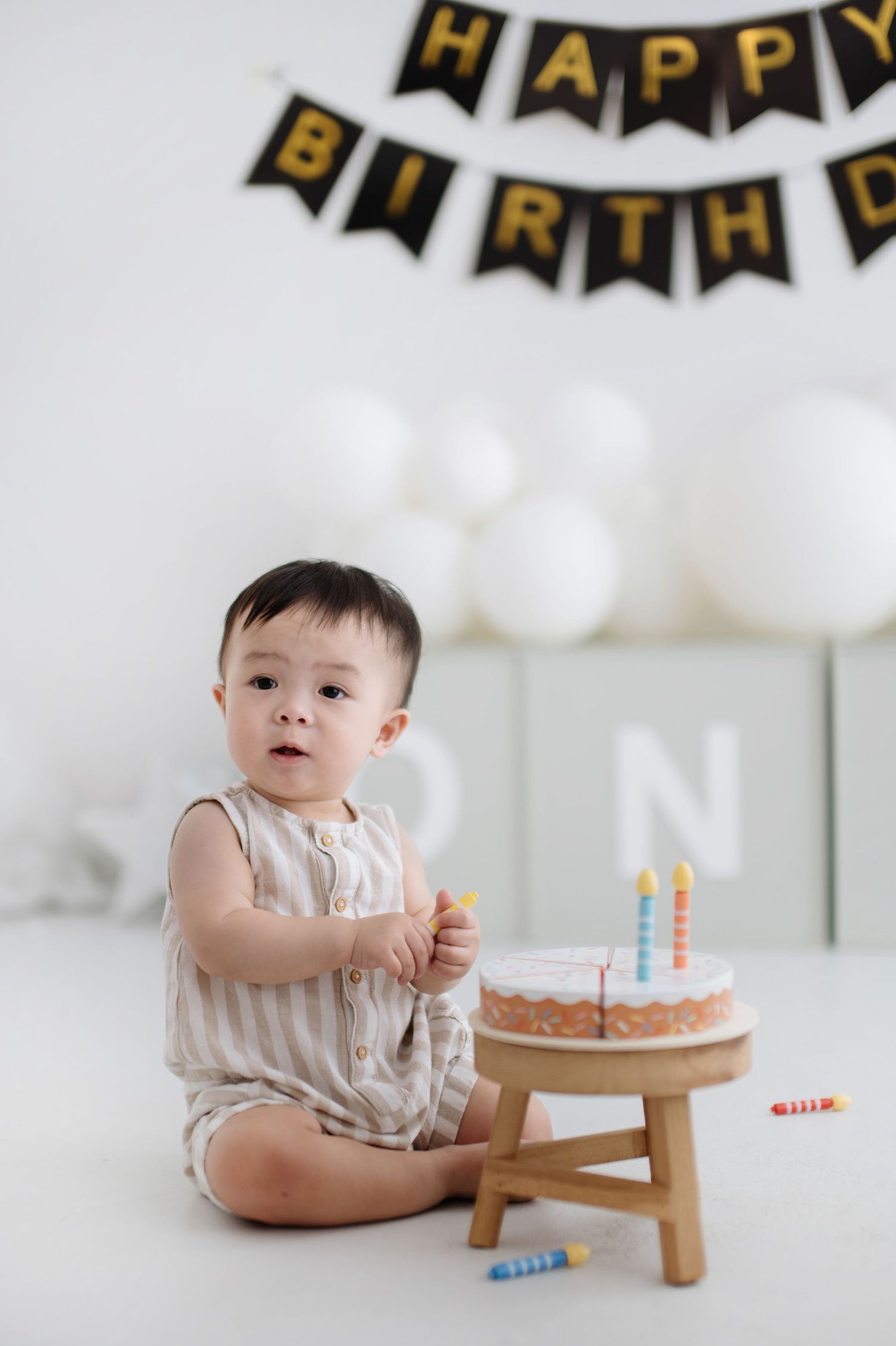 Birthday celebration setup with black and gold banners, small wooden stool, and cake for a first birthday party.