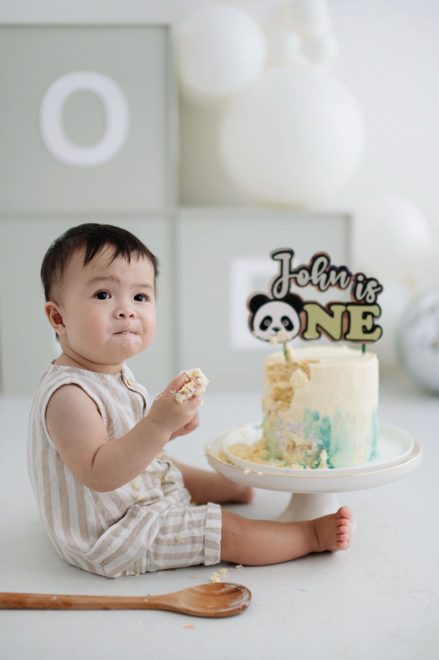 A first birthday celebration with a panda-themed cake on a white pedestal and festive balloon decorations.