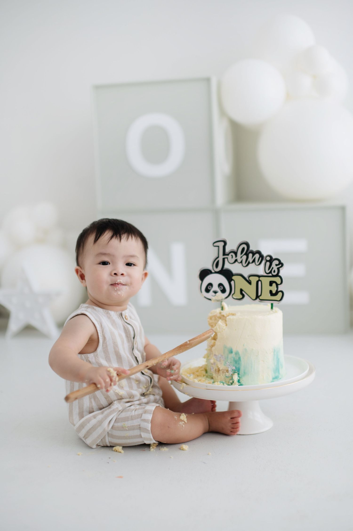 A one year birthday setup featuring a blue and white cake with panda topper and wooden spoon.