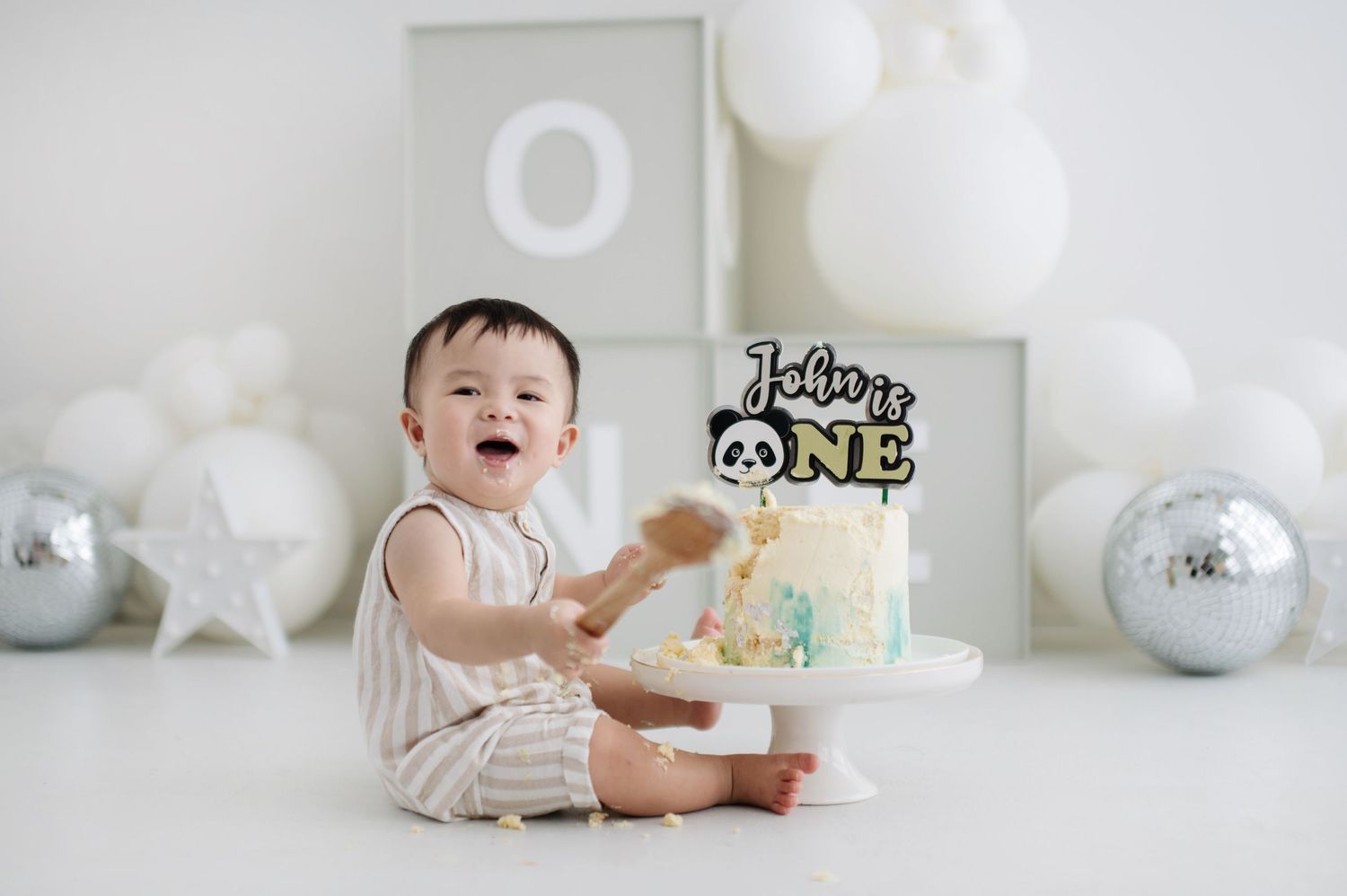 White minimalist cake smash setup with balloons and decorations for first birthday celebration.