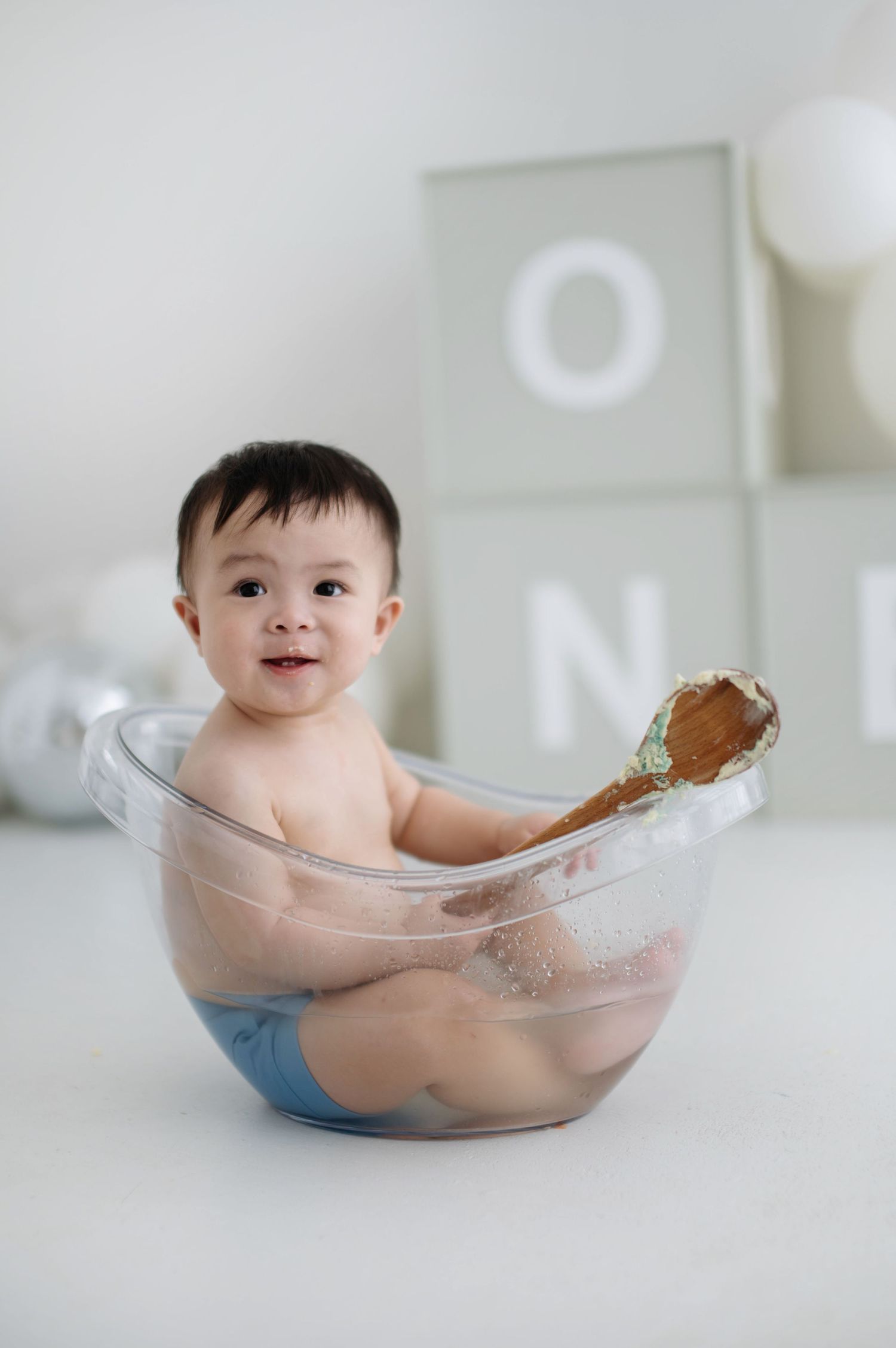 A playful bath time scene with clear tub, white bubbles and minimalist decor in the background.
