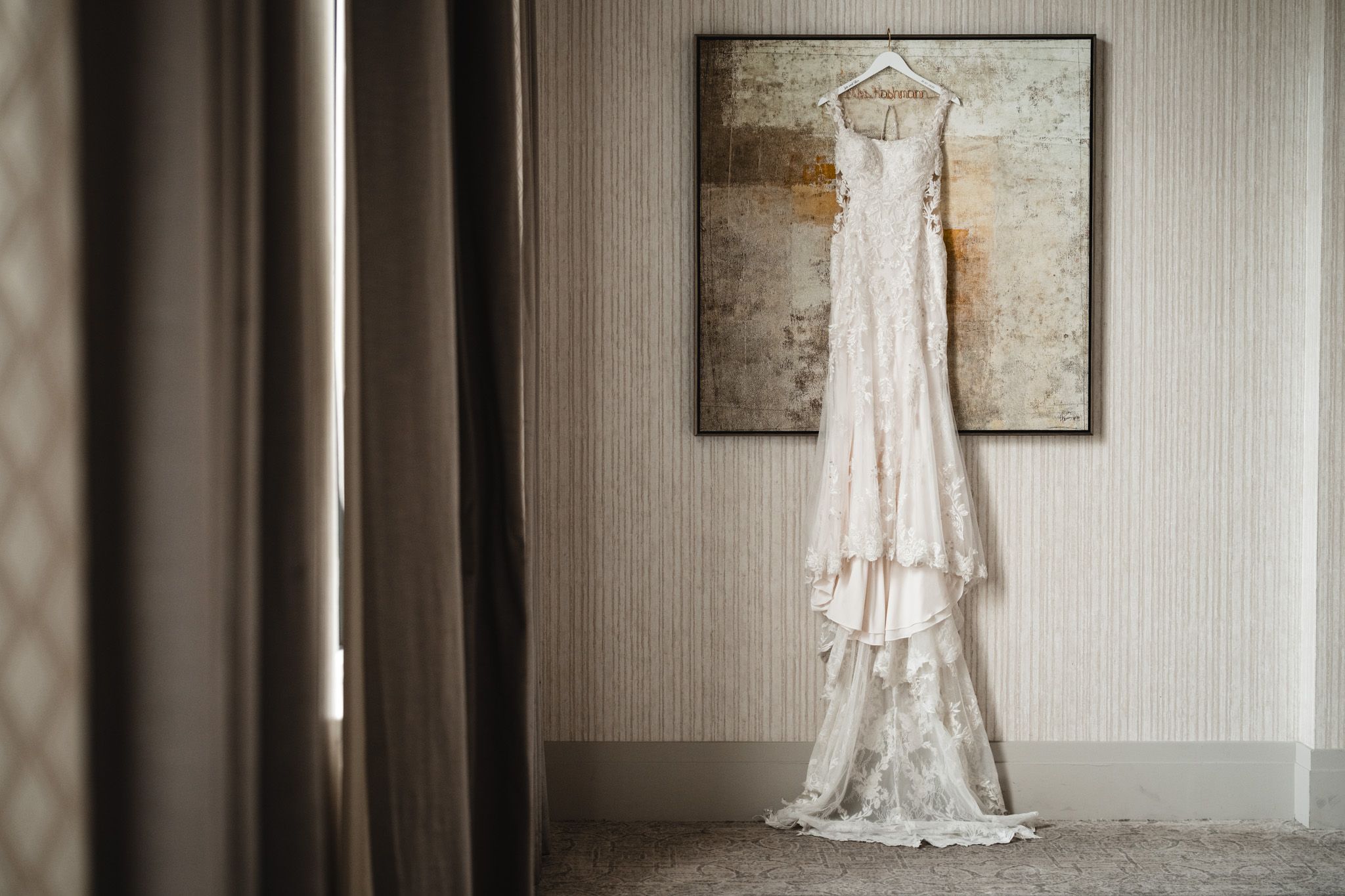 Wedding dress hanging elegantly in a bridal suite with minimalist decor.