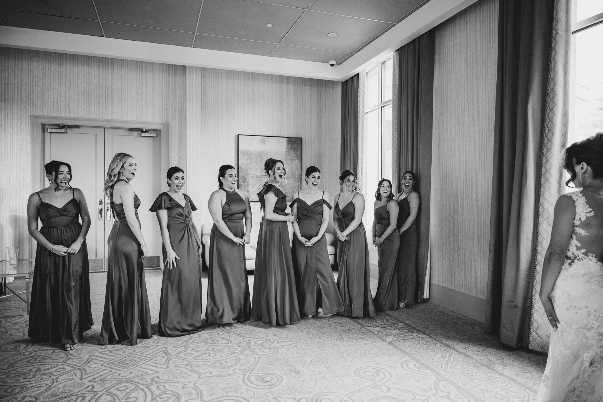 Wedding party in gray dresses lined up along hallway wall creating symmetrical composition.