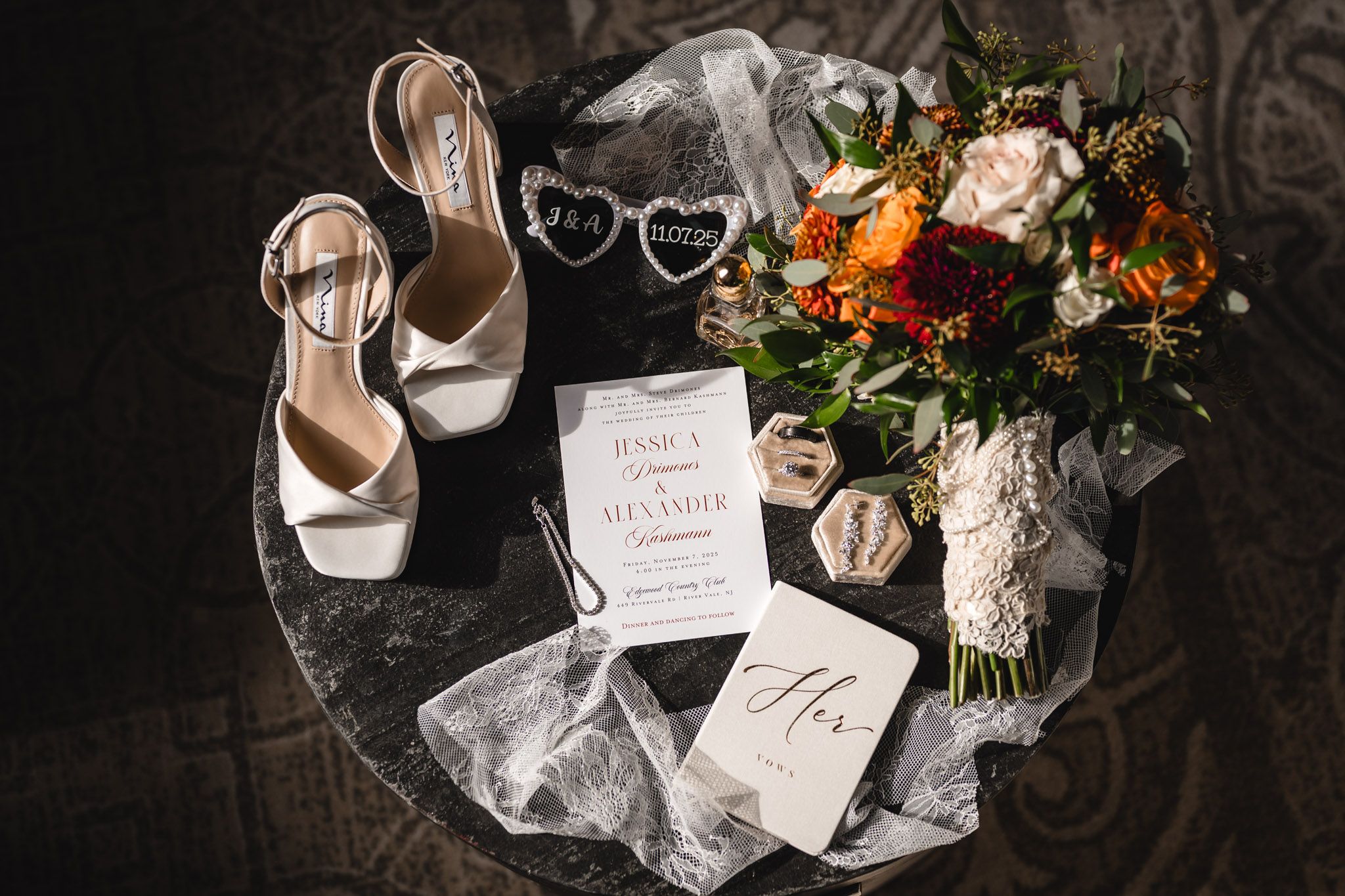 Wedding details including floral arrangements, invitations and bridal accessories on dark surface.
