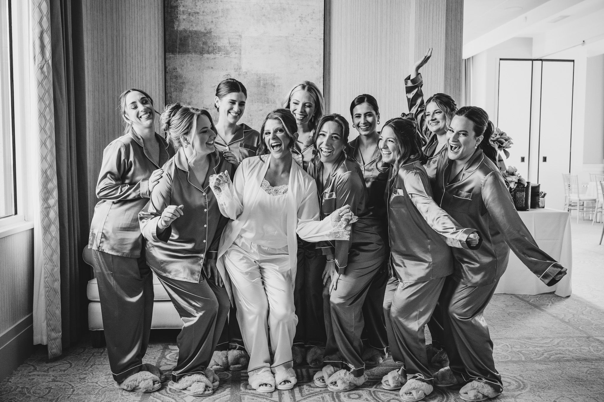 Bridesmaids in black dresses sit in a row showing emotional reactions during a wedding day moment.