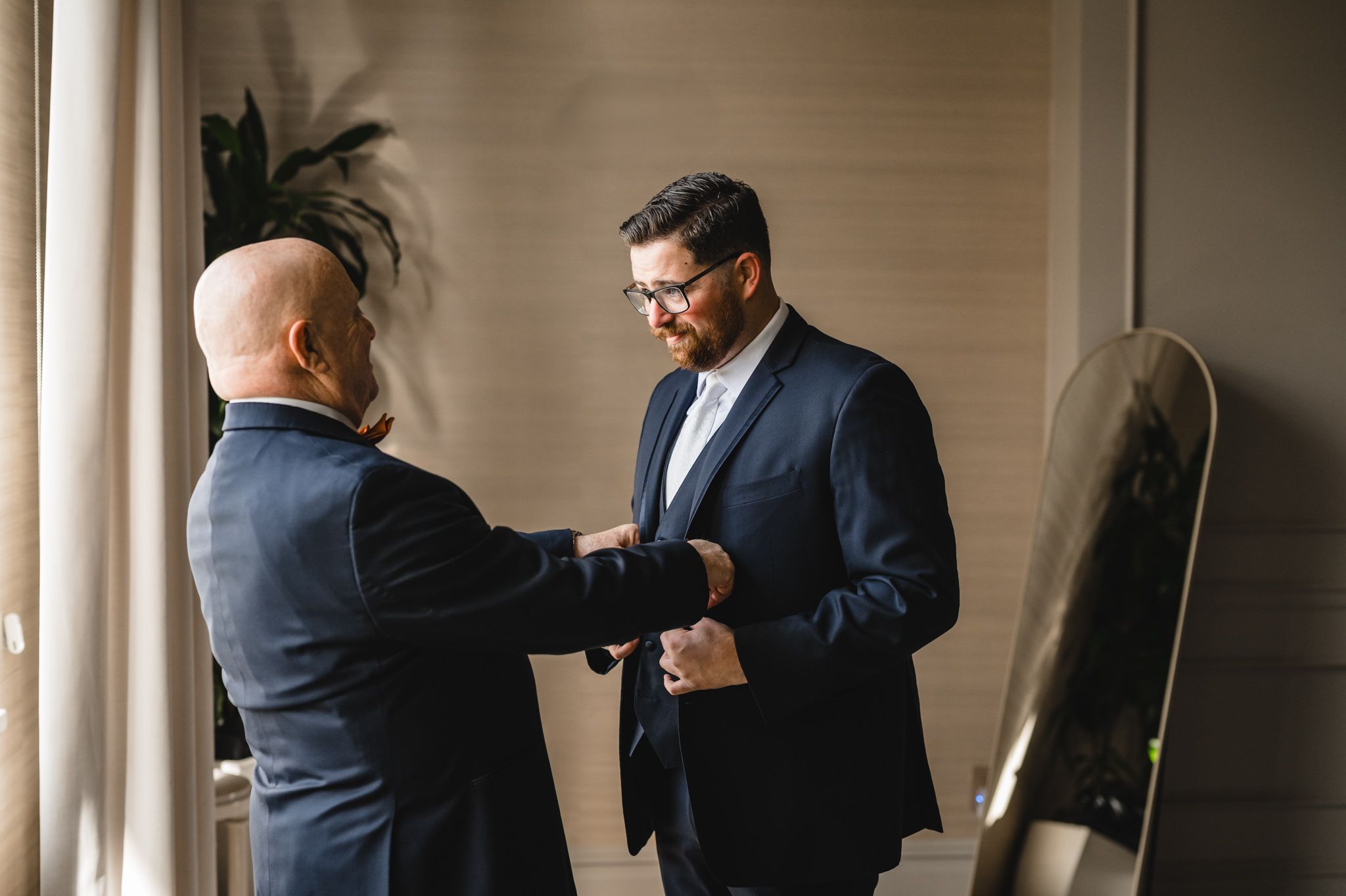 Men in formal suits preparing for a wedding ceremony in a minimalist indoor setting.