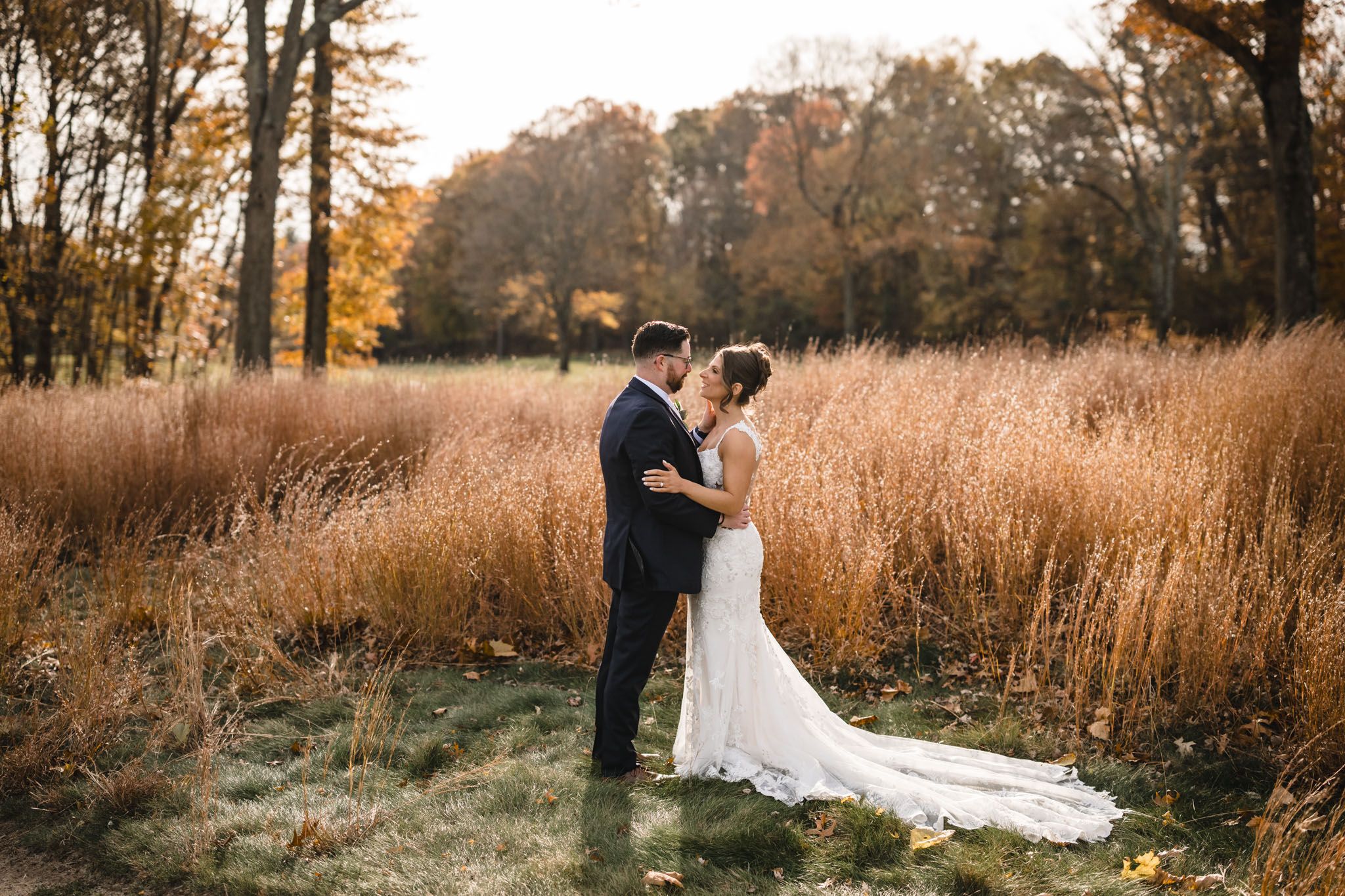 Elegant wedding couple stands together in golden autumn field during sunset.