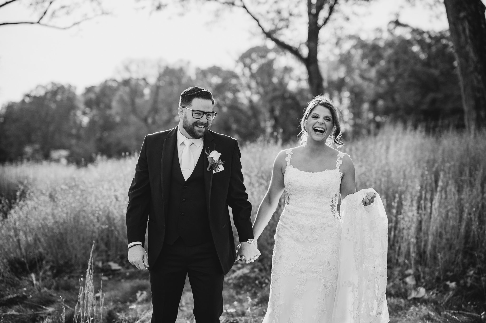 Elegant couple walks hand in hand through autumn field during wedding photoshoot.