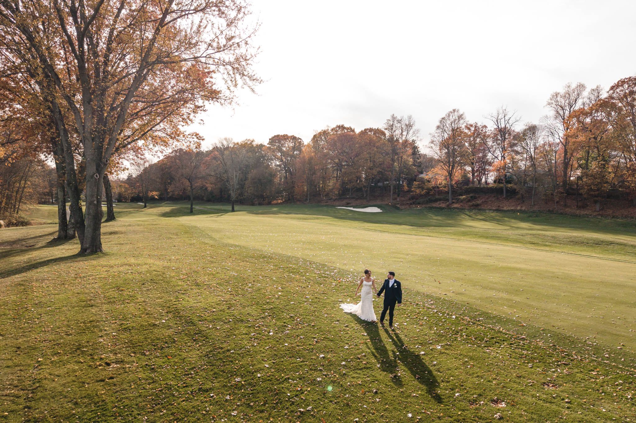Wedding couple walks across expansive golf course during golden hour.