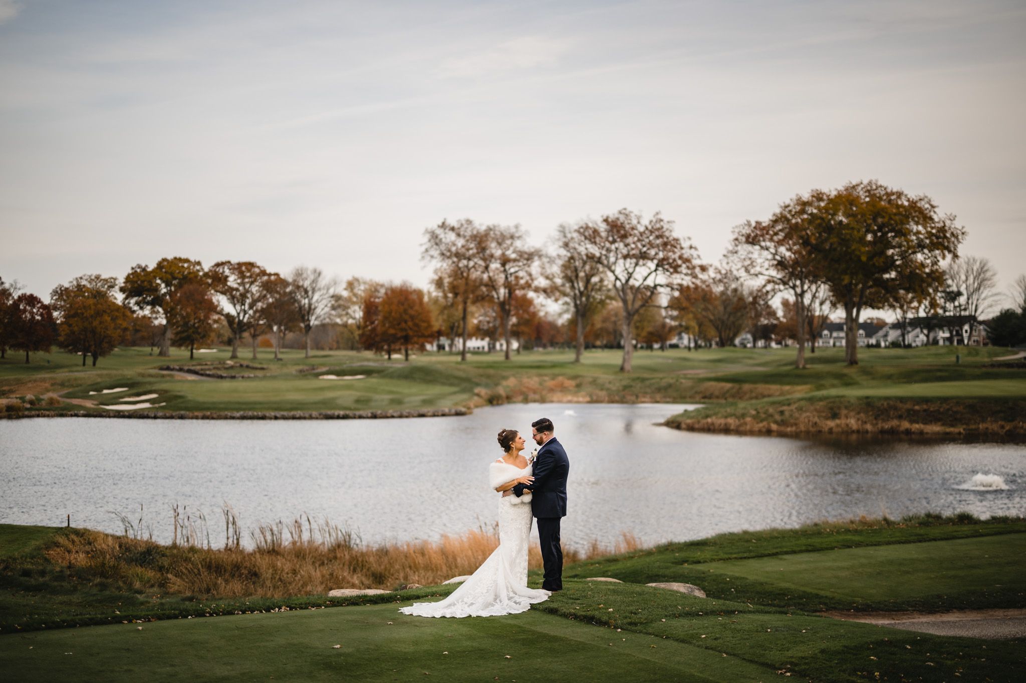 Panoramic view of a golf course wedding venue with a lake and autumn trees in the background.