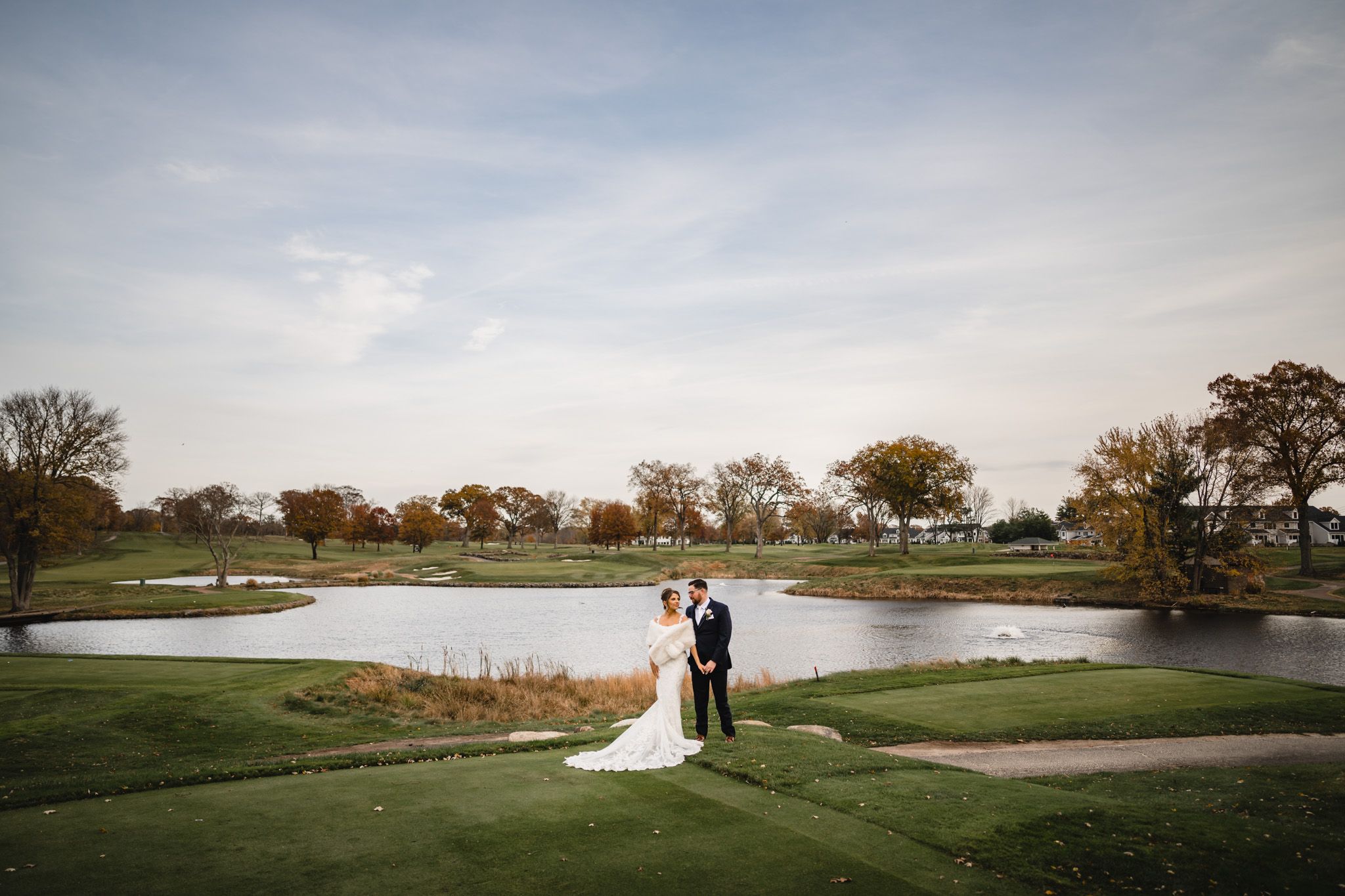 Wedding couple poses for romantic photos along a lakeside golf course at sunset.