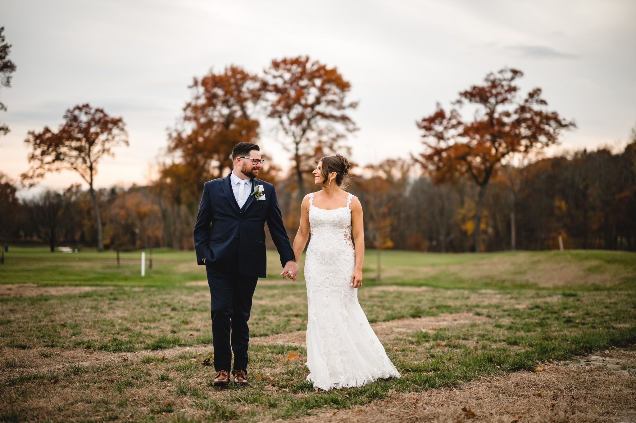Couple taking wedding photos on a scenic golf course with fall foliage in the background.