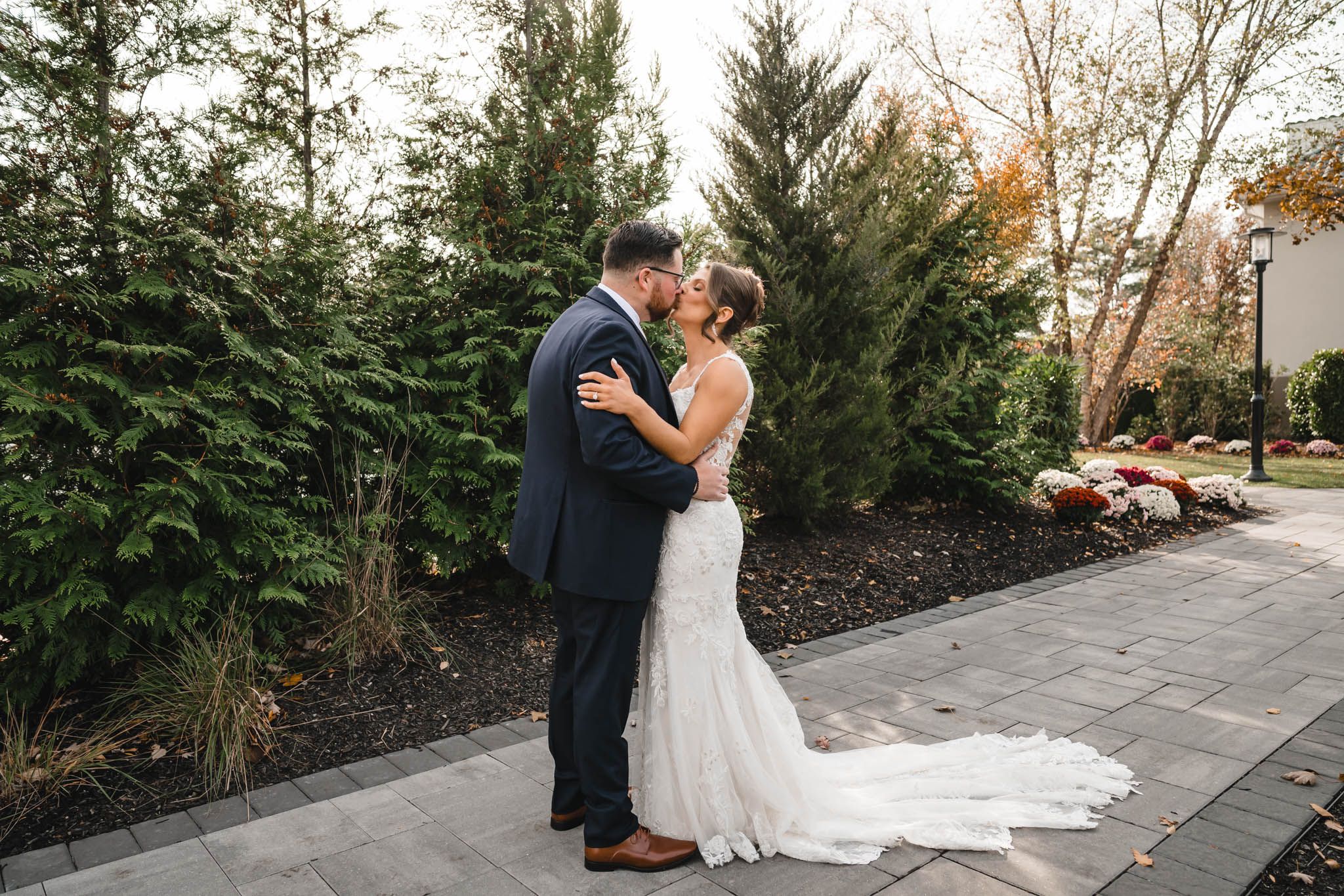 Wedding couple embracing on stone pathway surrounded by landscaped gardens.
