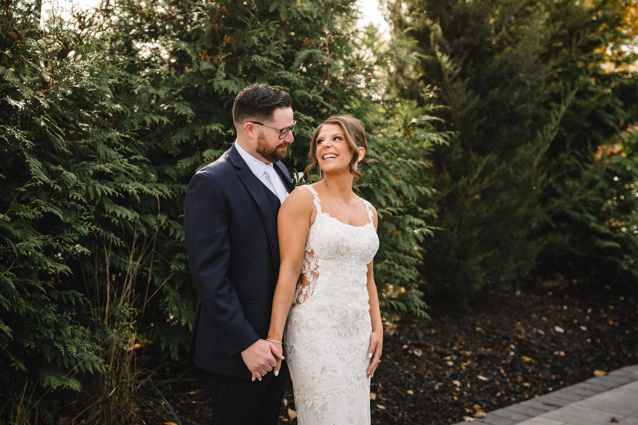 A romantic wedding couple poses together in a lush outdoor garden setting at sunset.