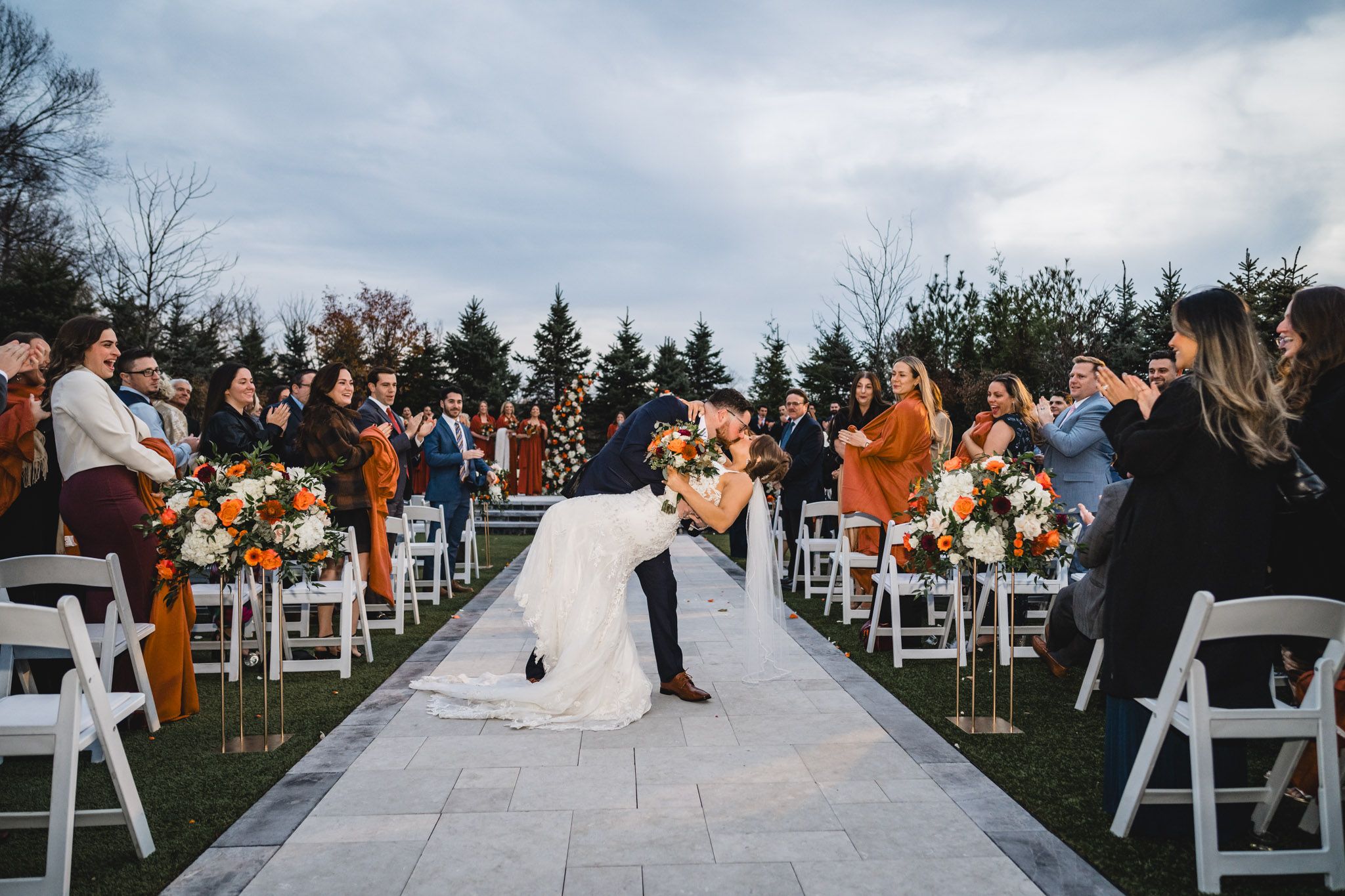 Wedding ceremony exit with guests seated on white chairs along outdoor aisle.