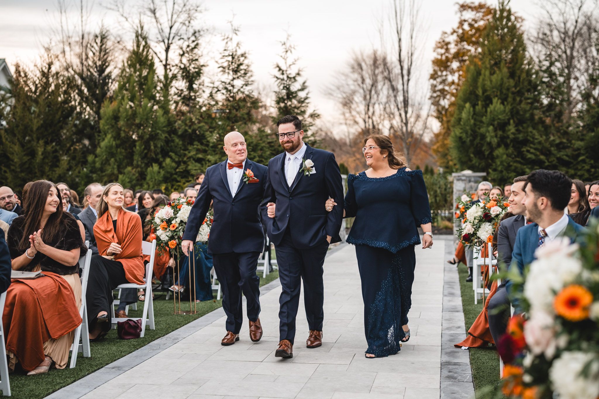 Wedding ceremony processional on an outdoor path with autumn decorations.