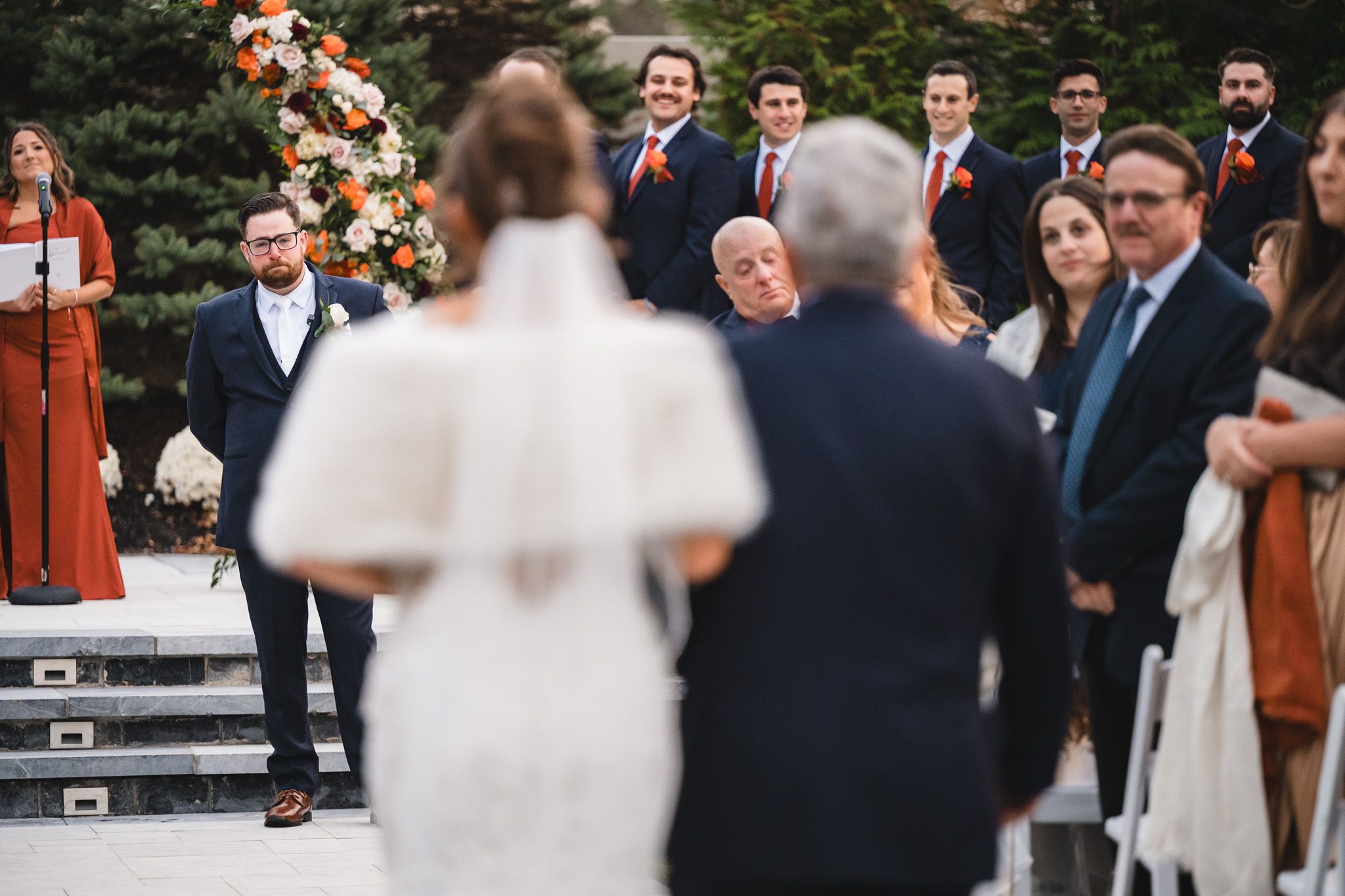 Wedding guests gather outdoors for ceremony with fall-themed floral arrangements.