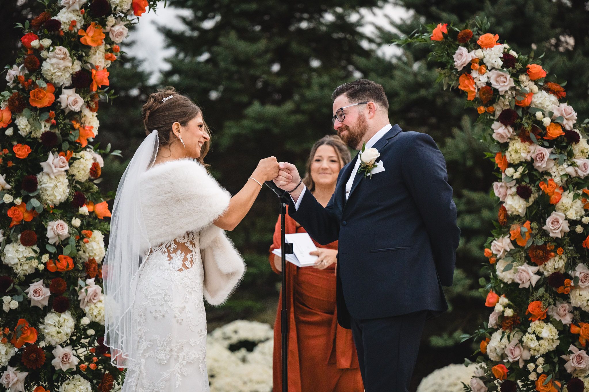 Outdoor wedding ceremony with elegant floral arch featuring orange and white blooms.