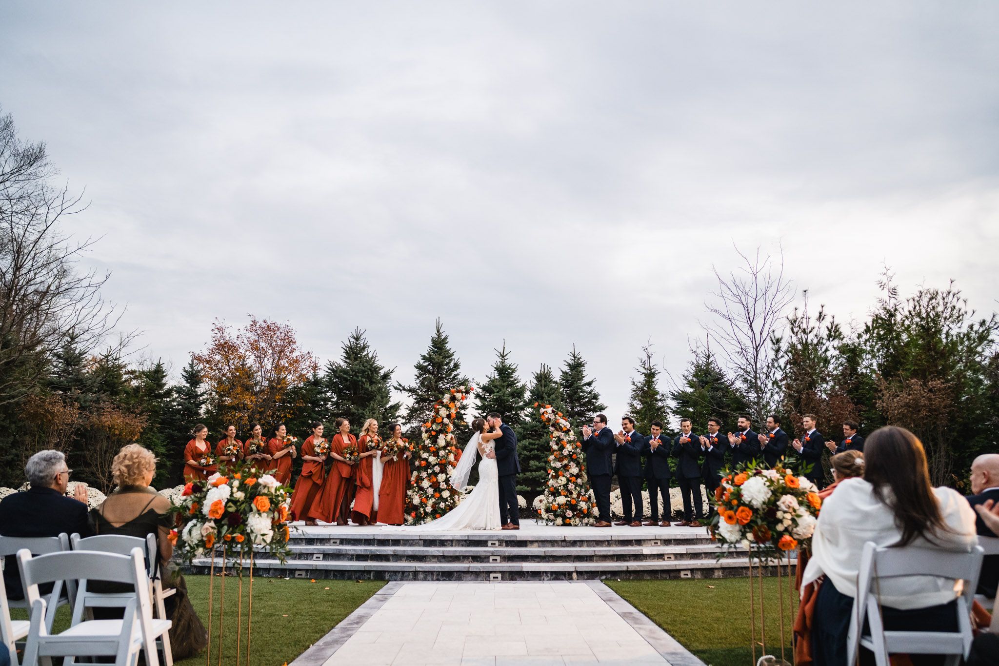 Wide angle view of wedding ceremony space with white chairs and autumn floral arrangements.