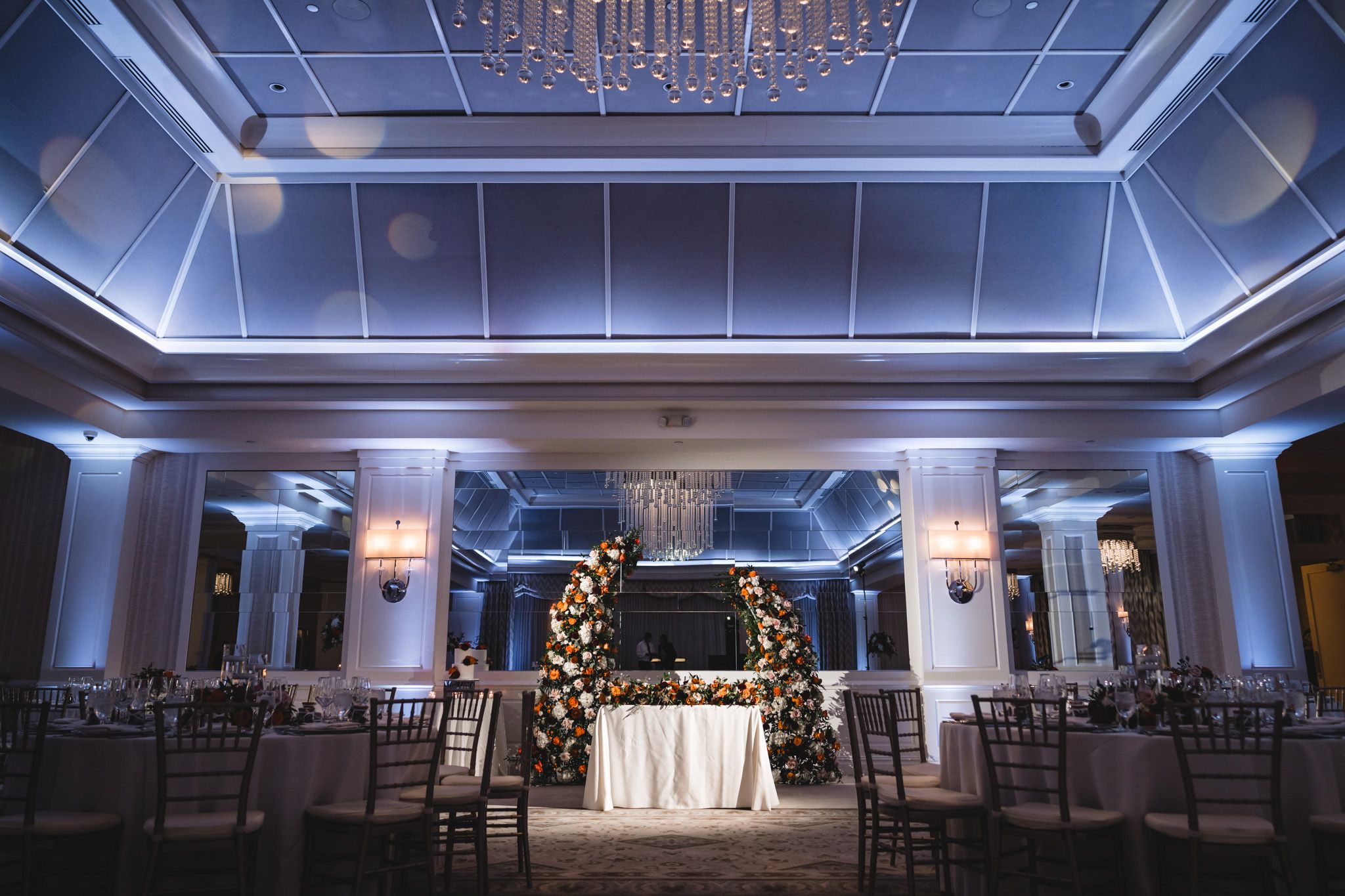 Elegant ballroom with blue uplighting and crystal chandelier ready for wedding reception.