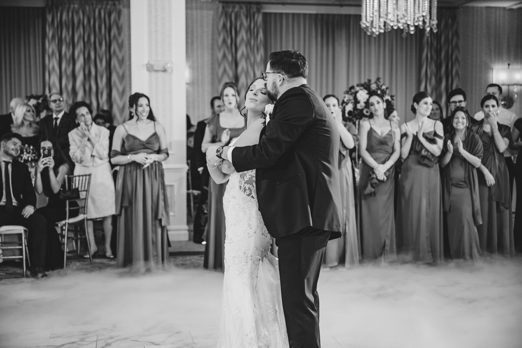 Wedding party and guests gathered in a grand ballroom with crystal chandeliers.
