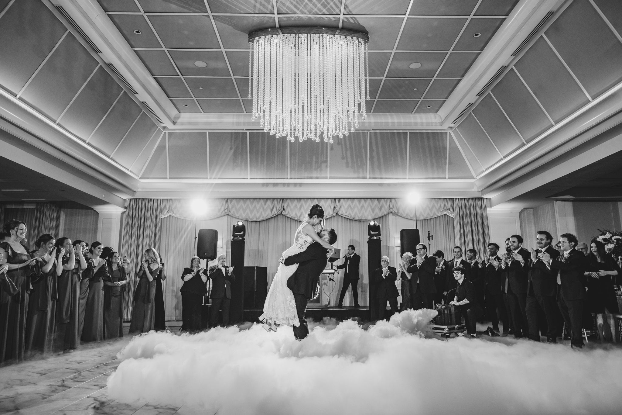 Wide angle view of a wedding reception with dramatic chandelier lighting and fog effects.