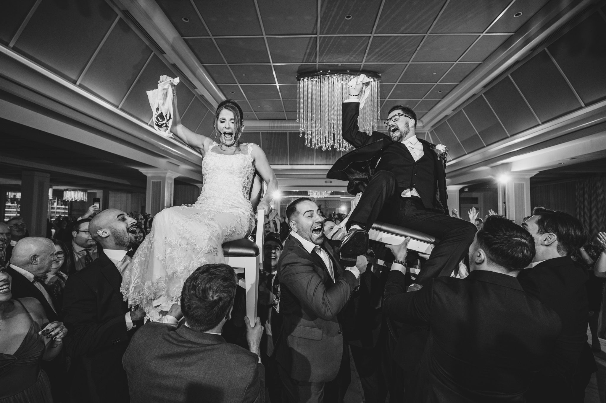 Wedding guests dance and celebrate on a lively dance floor under elegant chandeliers at an evening reception.