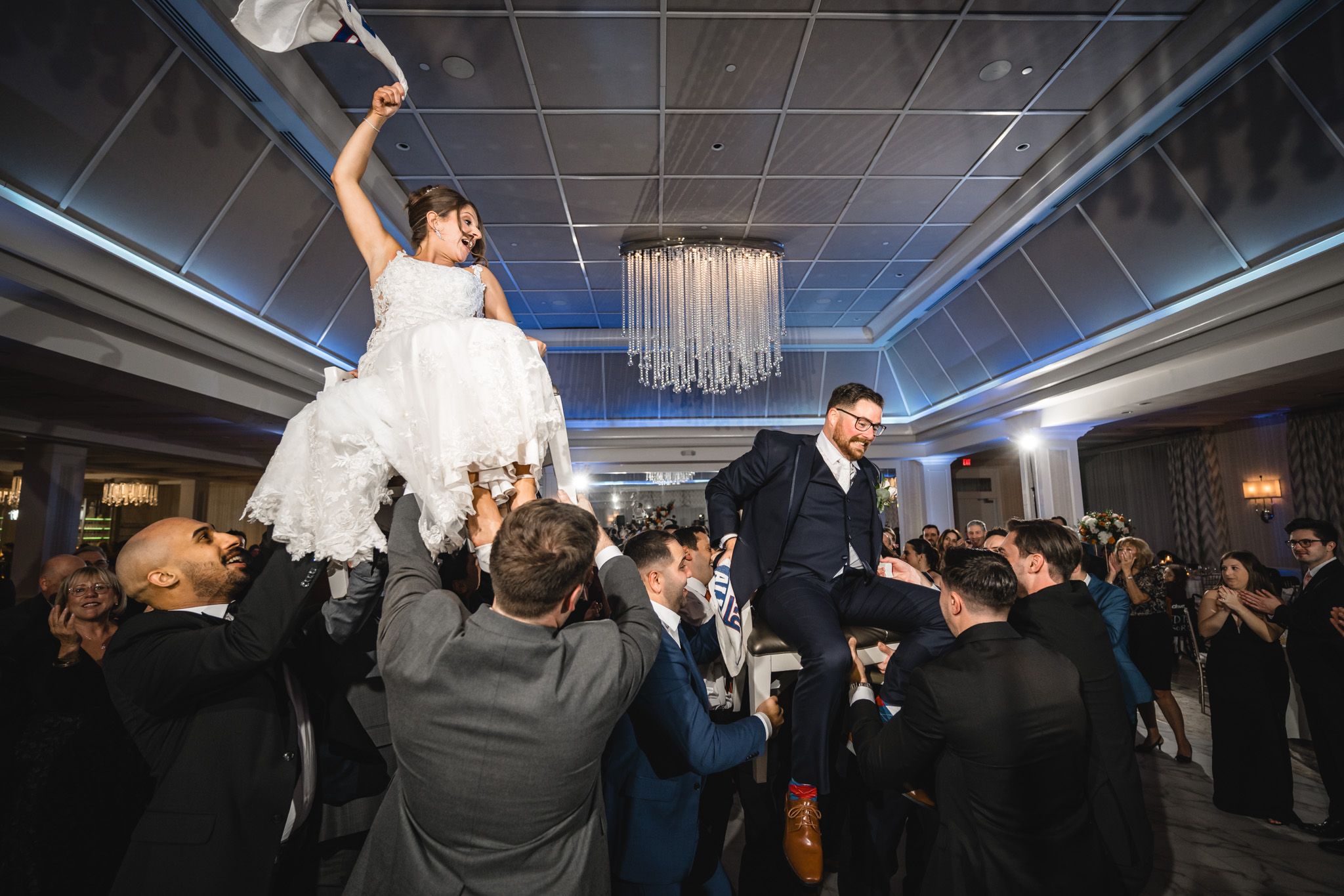 Energetic crowd dancing and celebrating at a wedding reception with blue accent lighting.