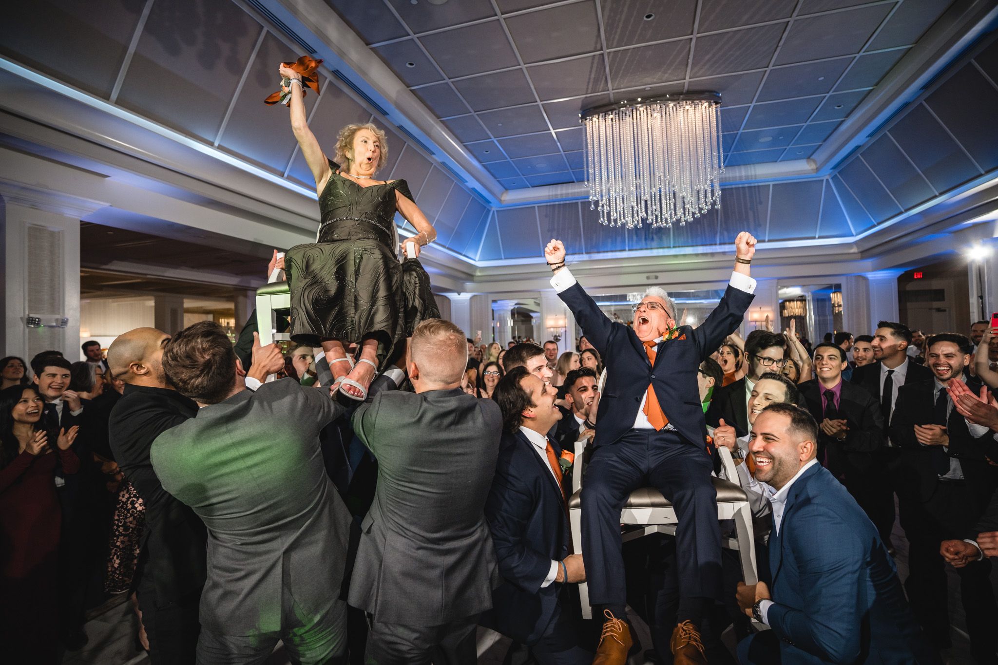 Wedding party celebrates with raised arms on dance floor under dramatic blue lighting.