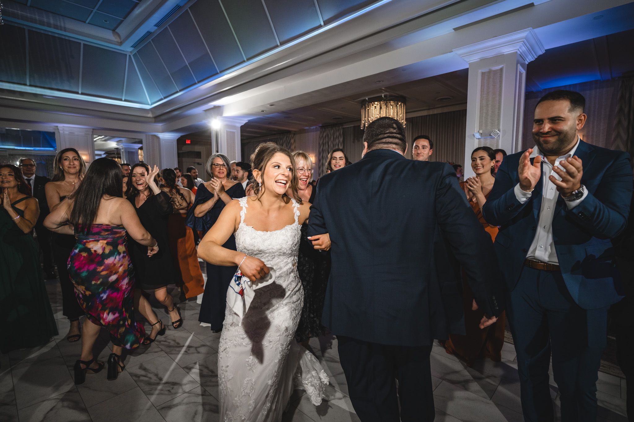 Guests dance and celebrate during a wedding reception with dramatic blue and purple lighting effects.