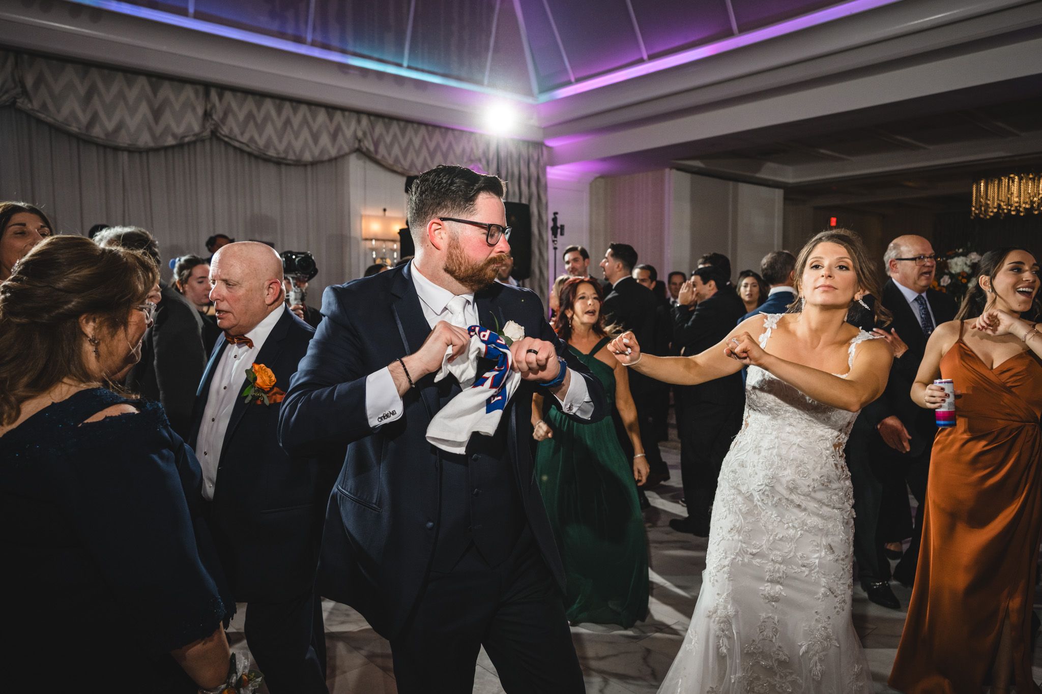 Wedding celebration in full swing with colorful mood lighting and chandelier in an elegant ballroom.