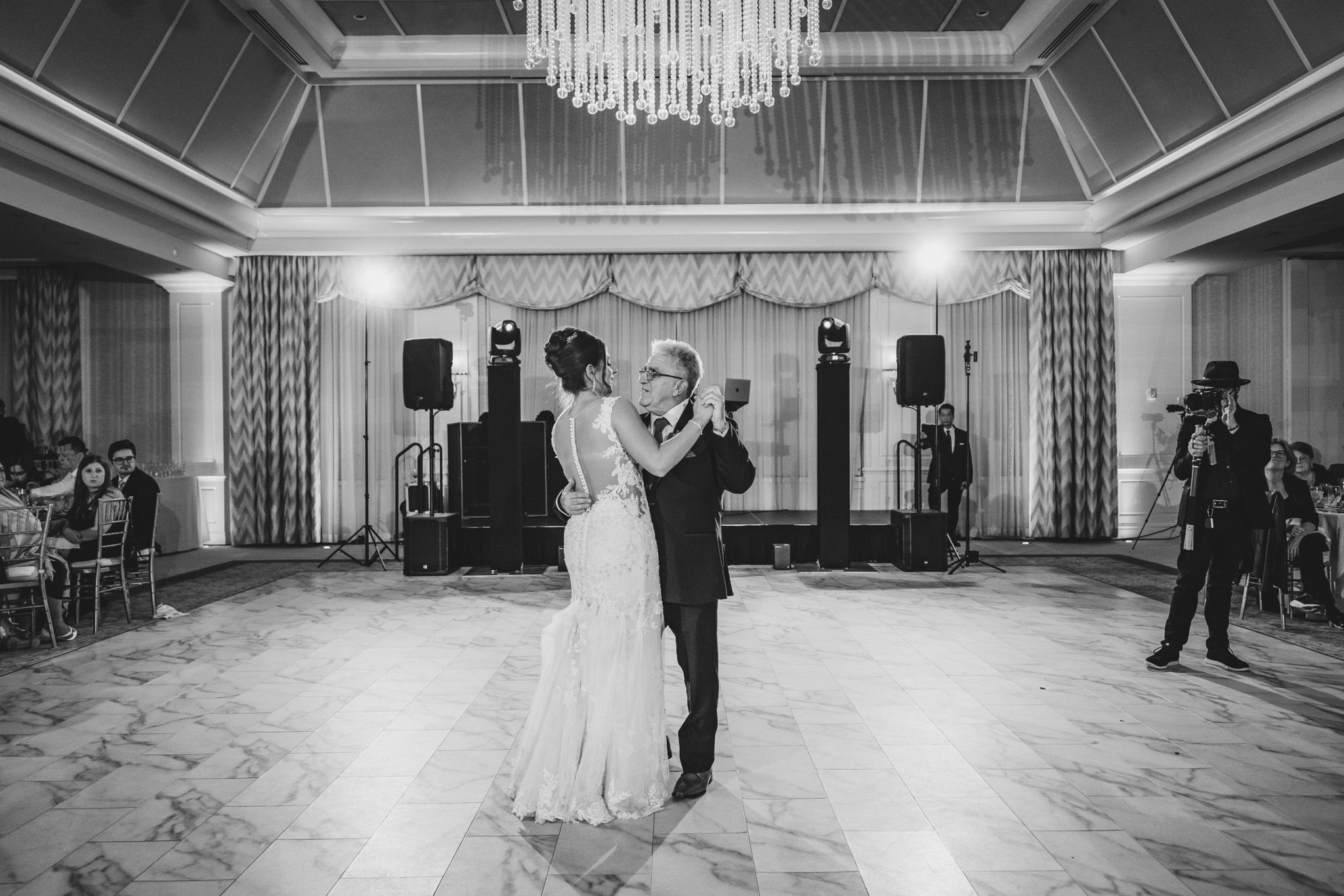 Elegant ballroom setup for wedding reception with crystal chandelier and dramatic lighting.