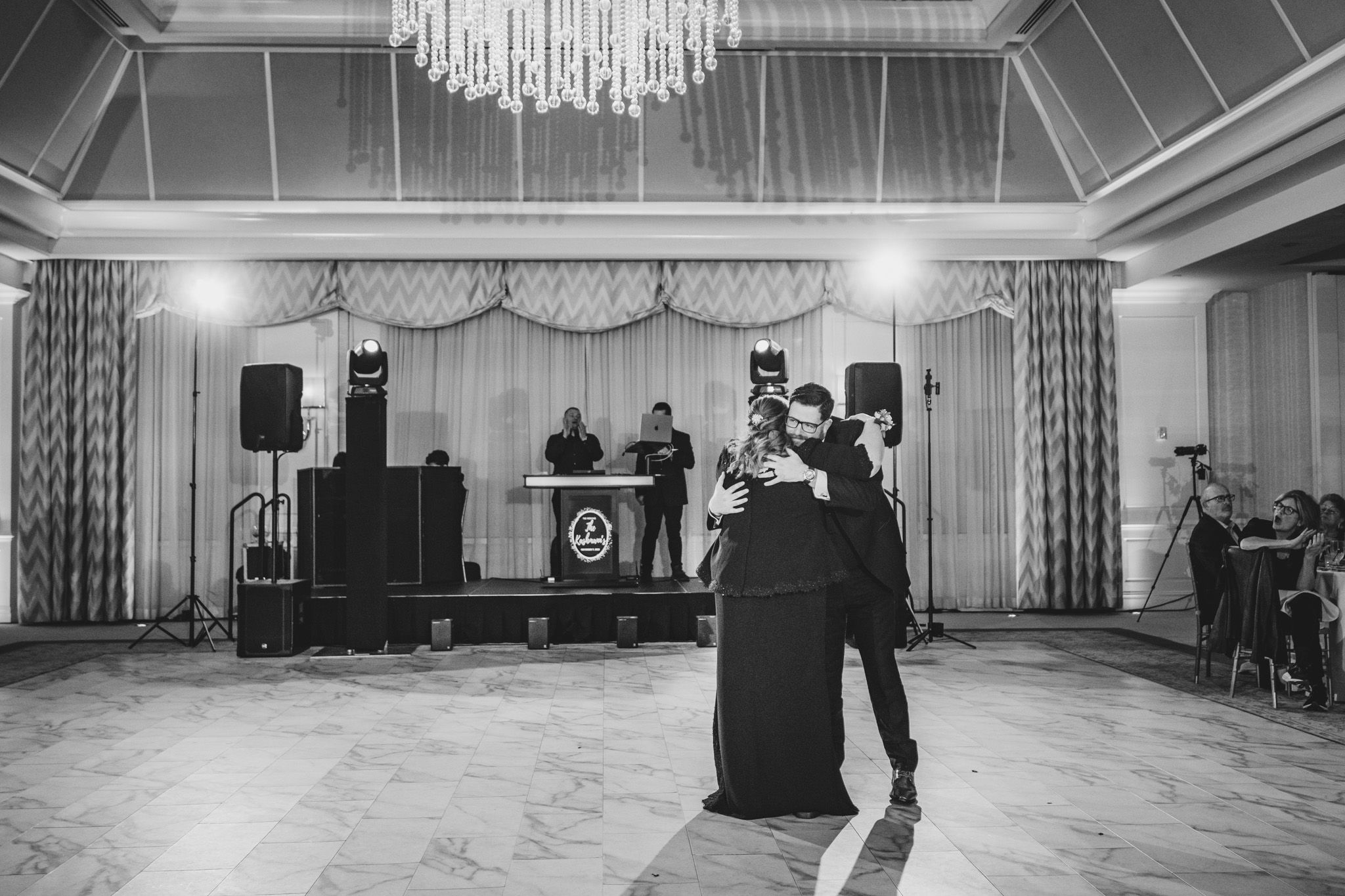 Wedding guests dance and celebrate on an elegant ballroom floor under a crystal chandelier.