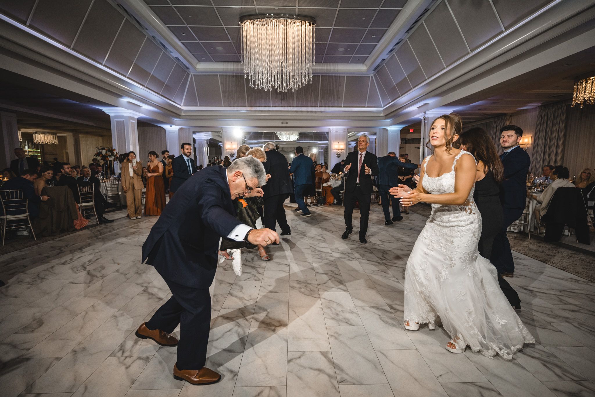 Couples dancing together at an elegant wedding reception under ornate chandeliers.