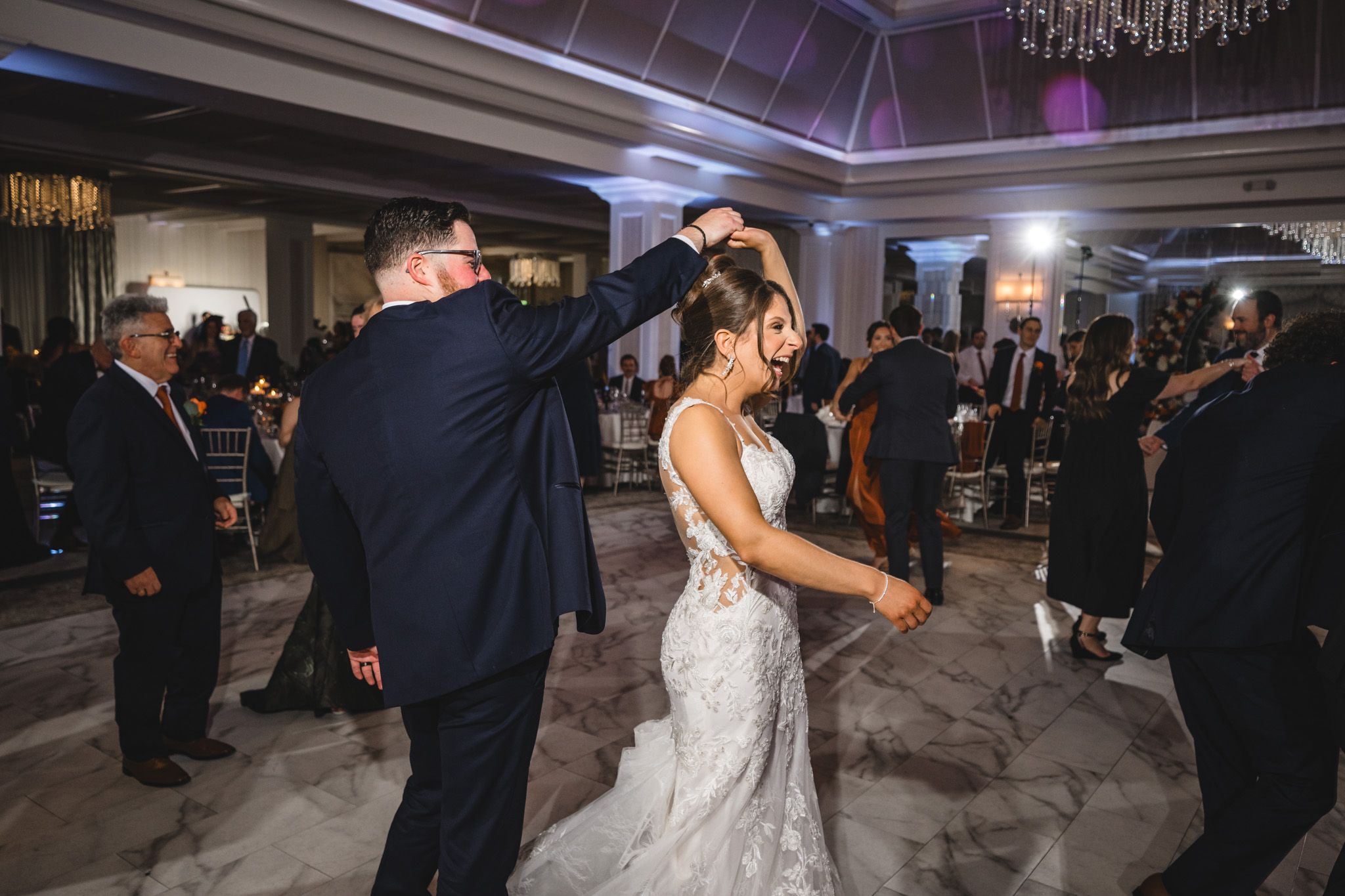Wedding party dancing and celebrating in a luxurious ballroom with mood lighting.