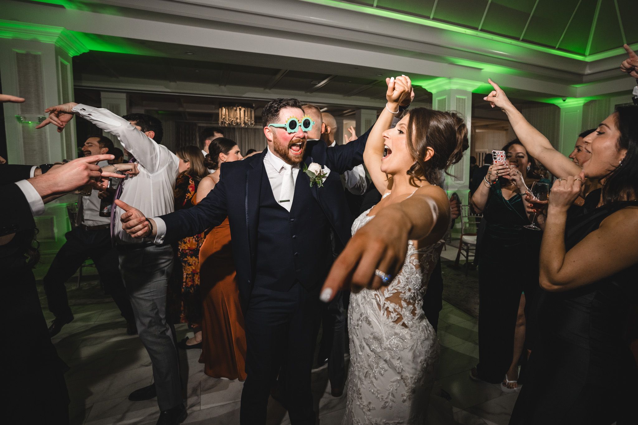Wedding reception dance floor illuminated with green lighting as guests celebrate.