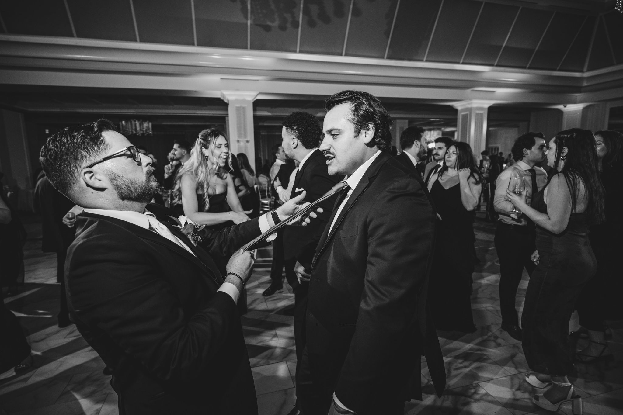Black and white photo of wedding guests dancing and celebrating at a reception.