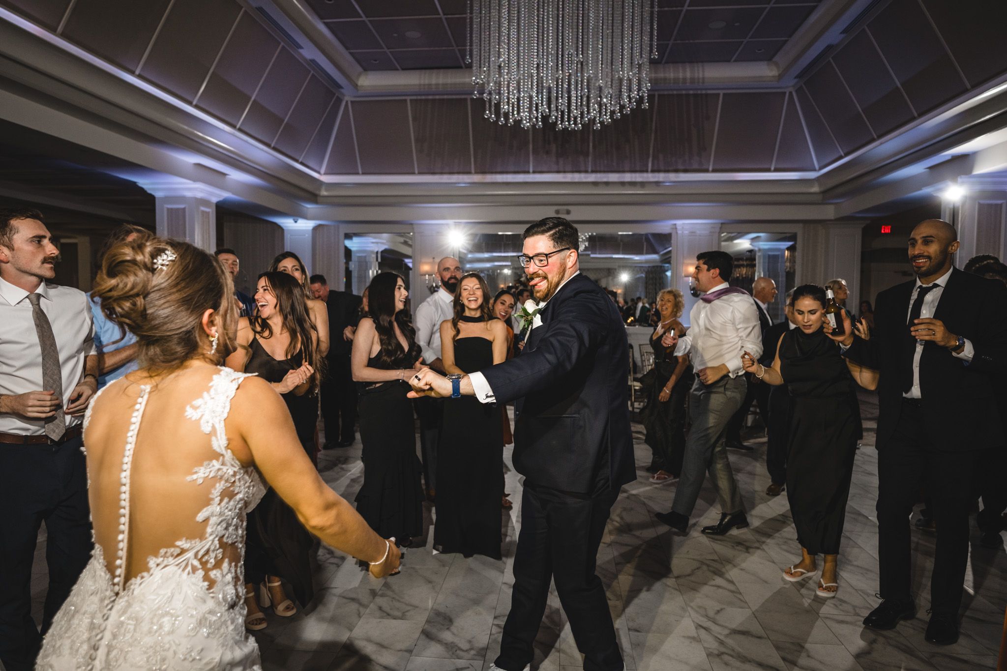 Wedding reception dance floor filled with guests under elegant chandelier lighting.
