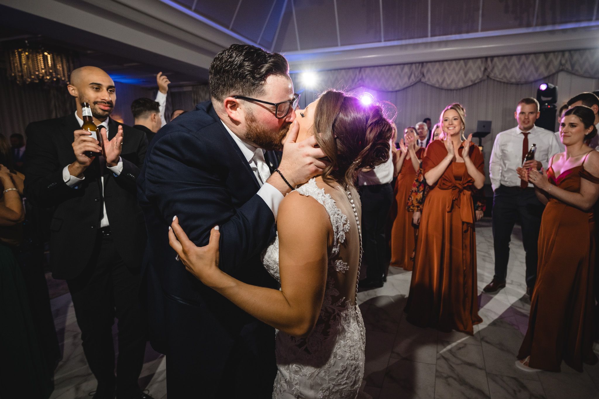 Energetic dance party at wedding reception with purple mood lighting.