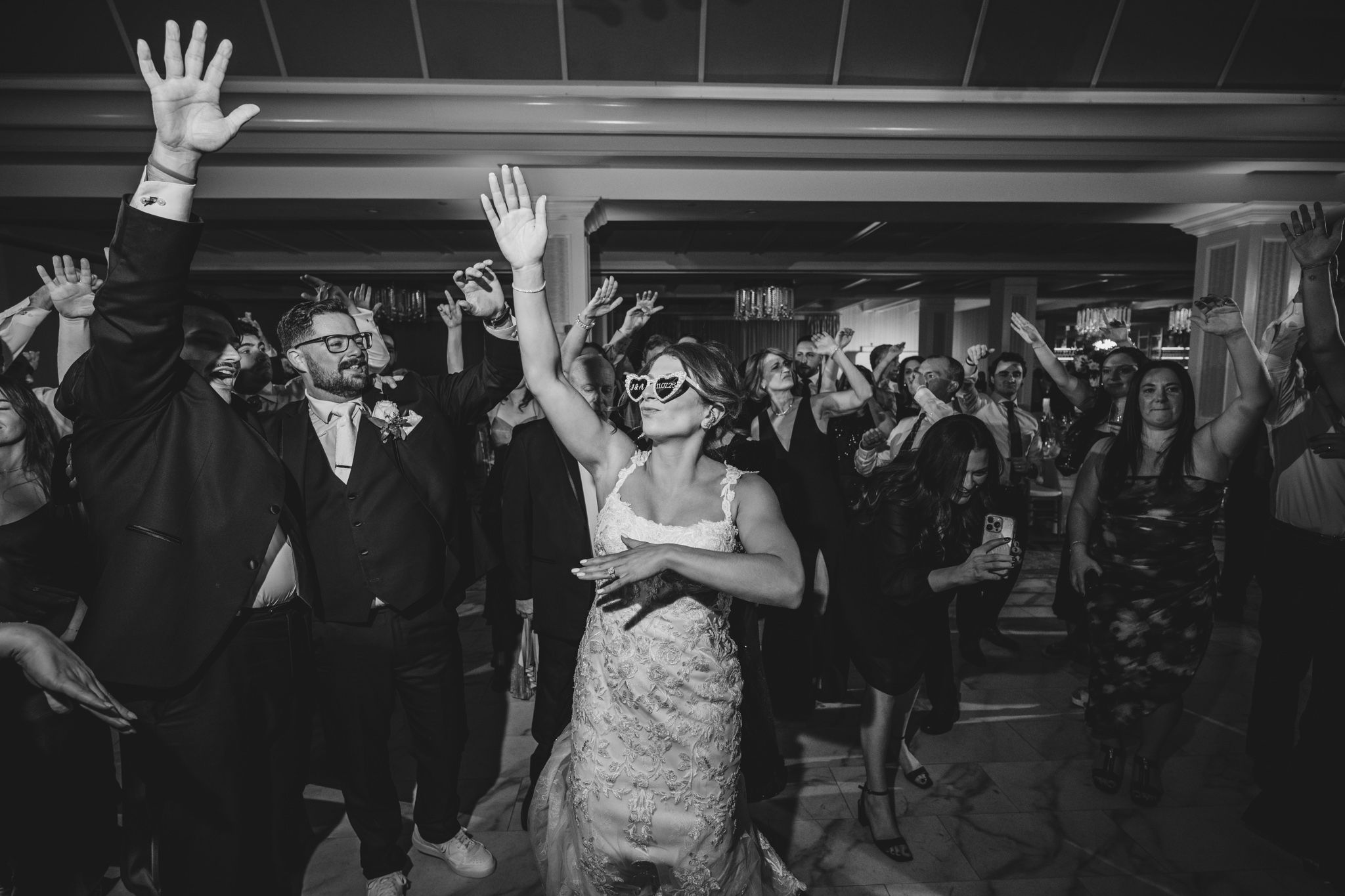 Wedding guests raise their hands in celebration while dancing at an energetic reception party.
