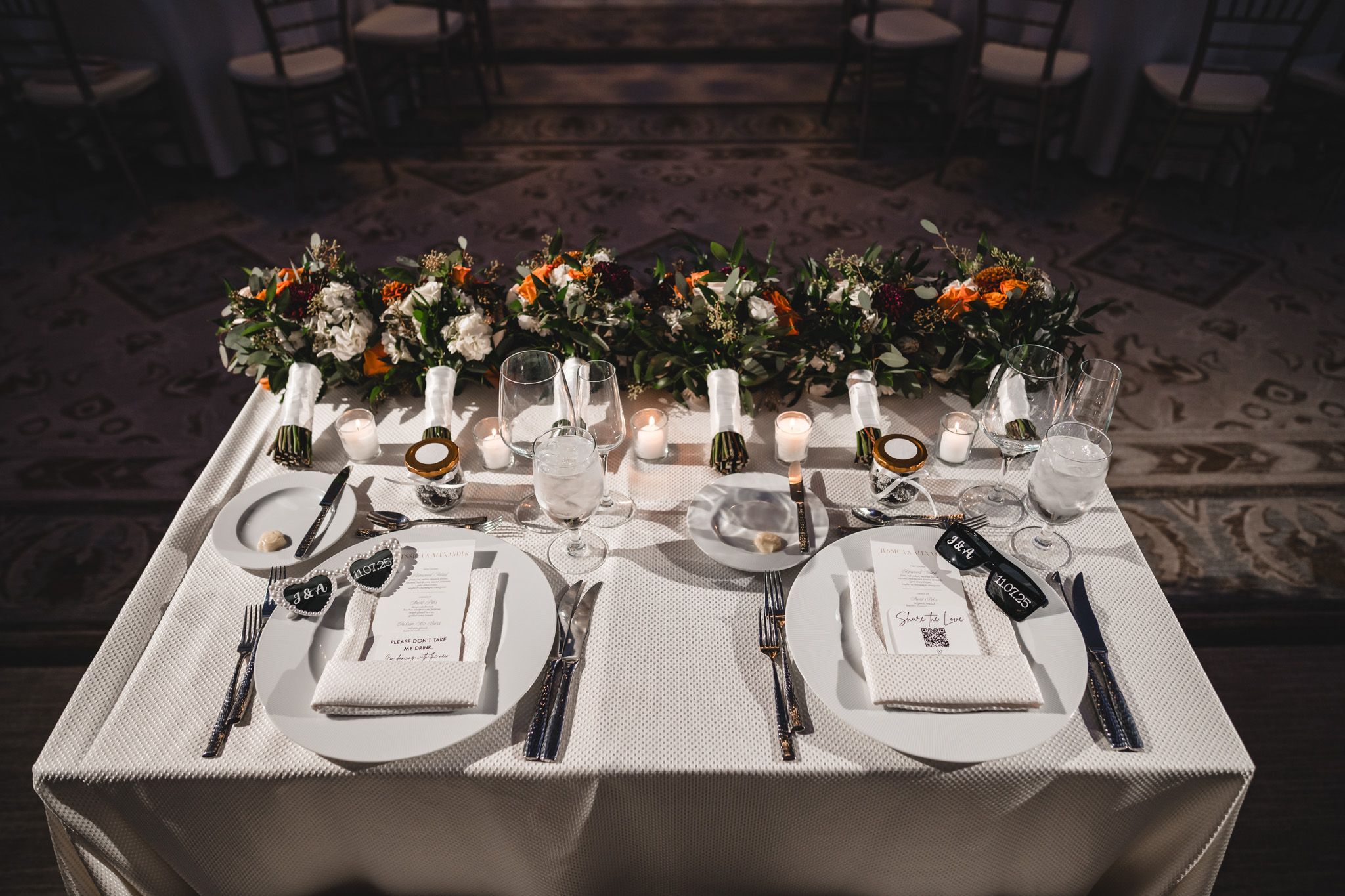 Long dining tables set with white linens and floral centerpieces in a dimly lit room.