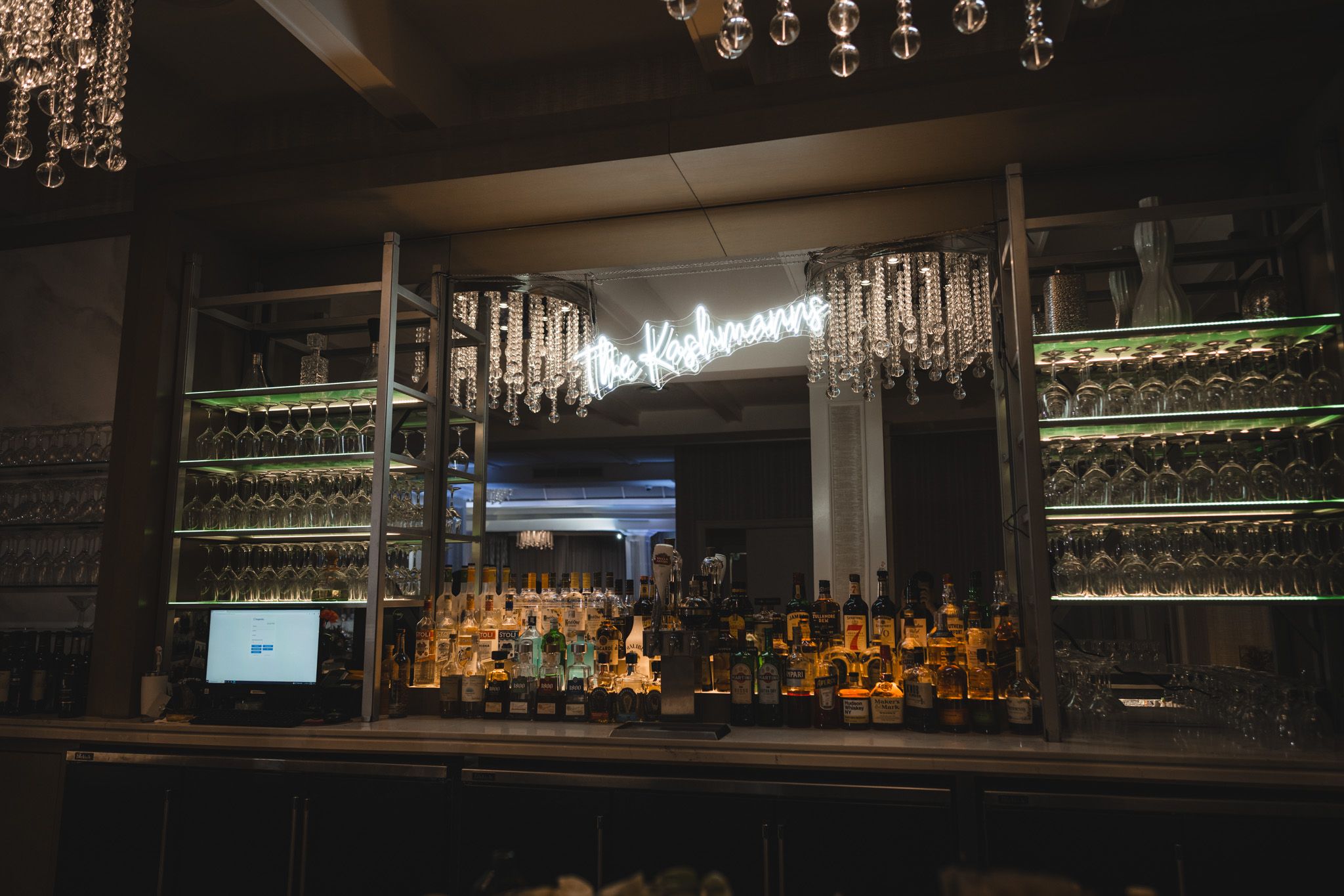 Bar display with illuminated bottles and glassware in dark ambient lighting.