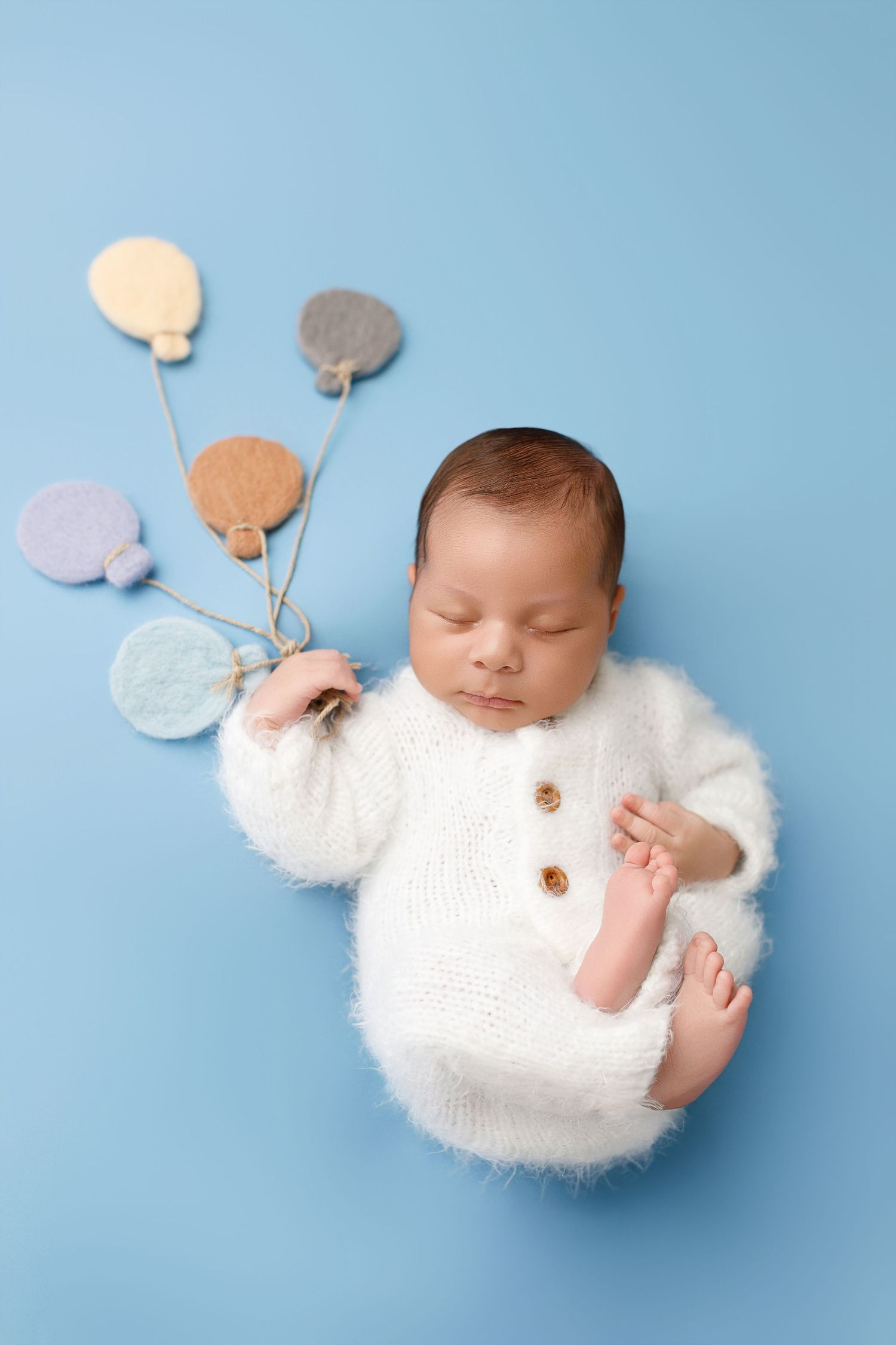 Sleeping baby wearing fluffy white sweater lying on blue background with decorative circles in artistic newborn photo.