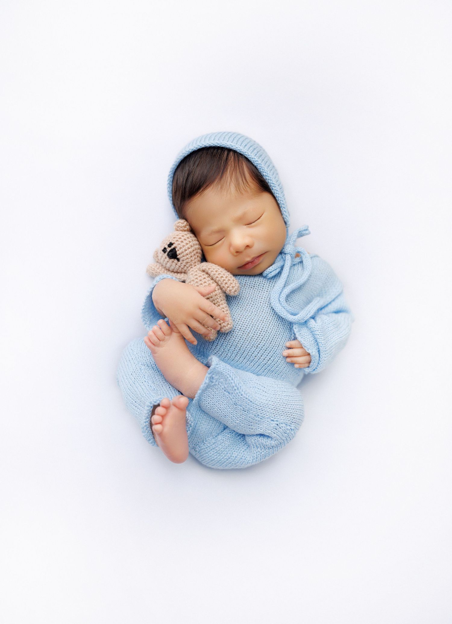 A sleeping baby in light blue clothing curled up in a peaceful pose on a white background.