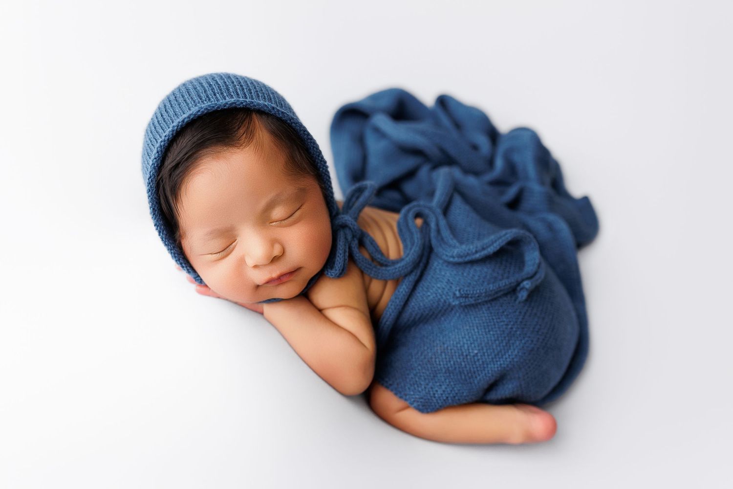 Sleeping newborn baby wrapped in soft blue swaddle blanket lying on white background.