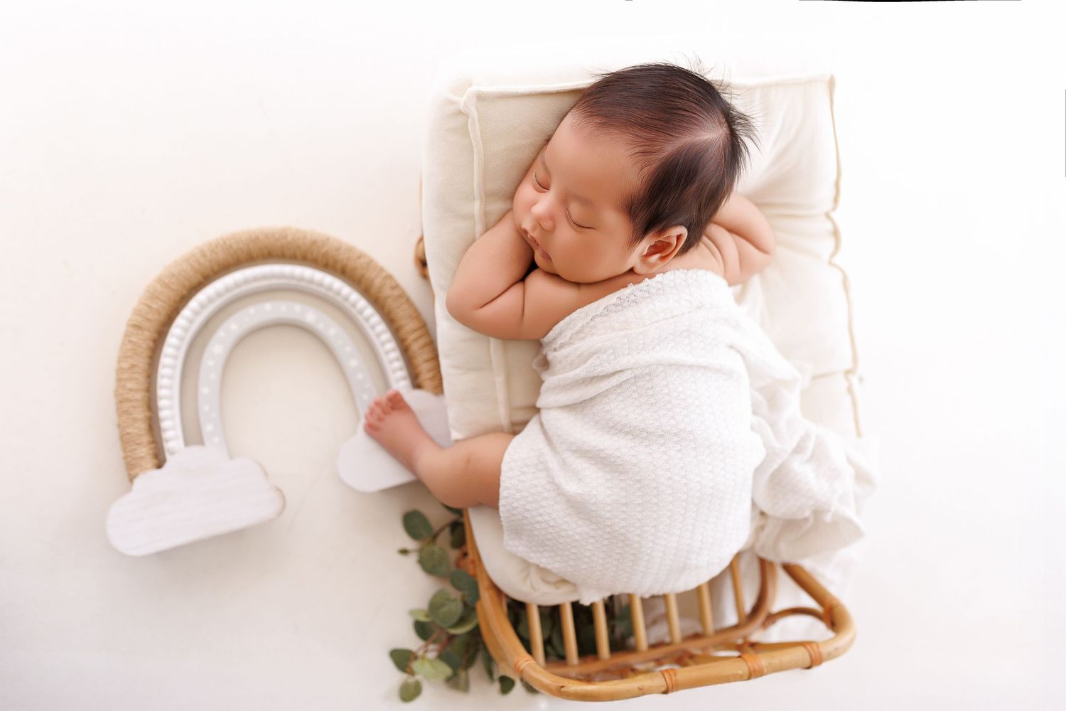 A sleeping baby in white clothing rests peacefully on a plush bed with white bedding and pillows.