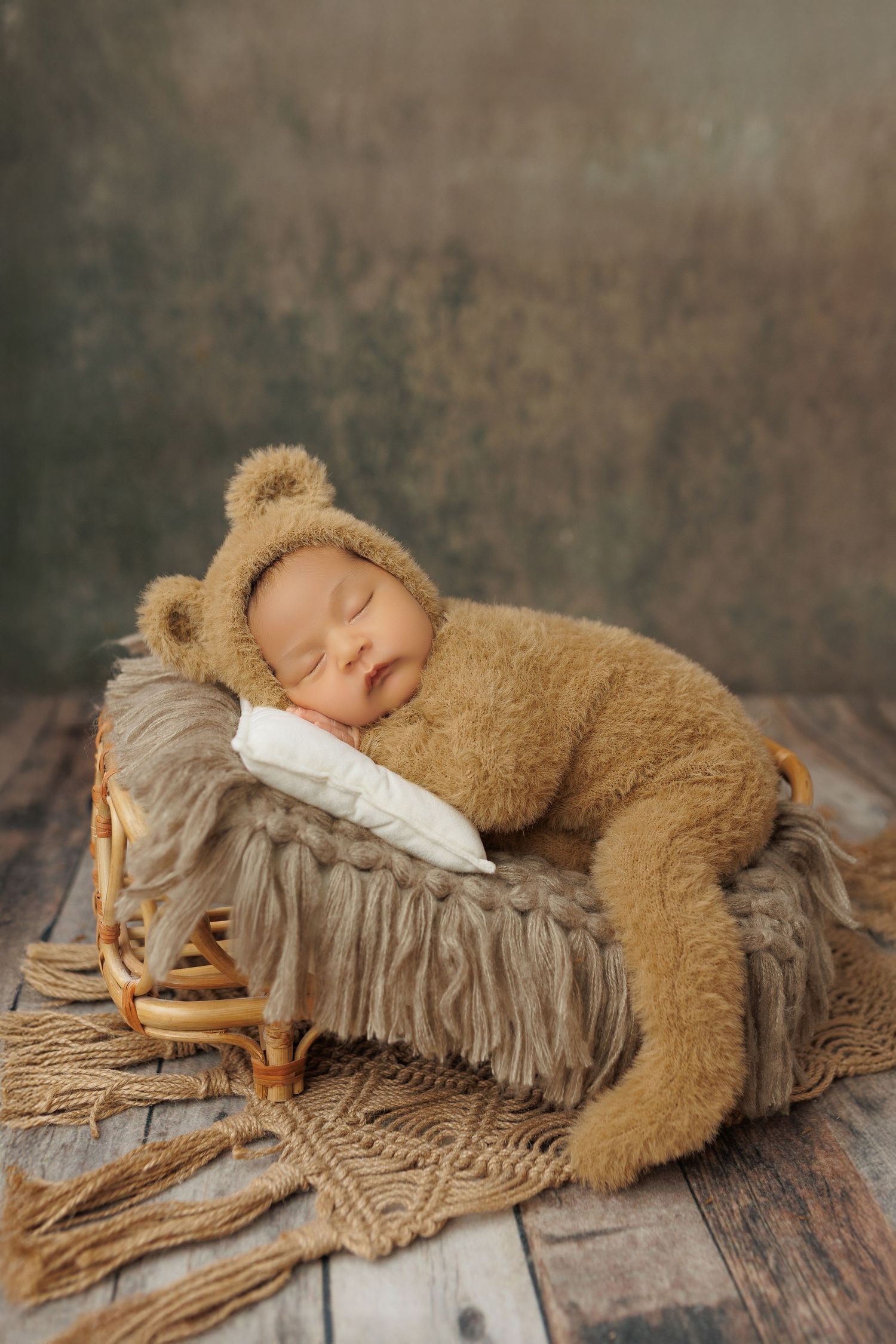 Sleeping newborn wearing cozy teddy bear costume rests on rustic wooden sled with textured blanket.