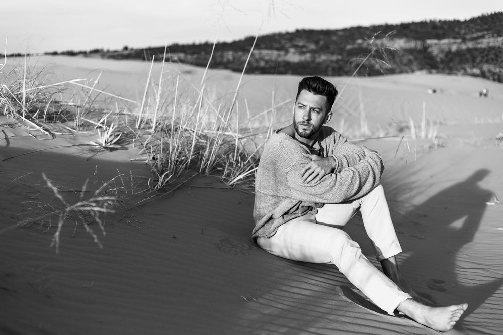 Person relaxing on sandy beach with tall grass and dunes in background during sunny day.