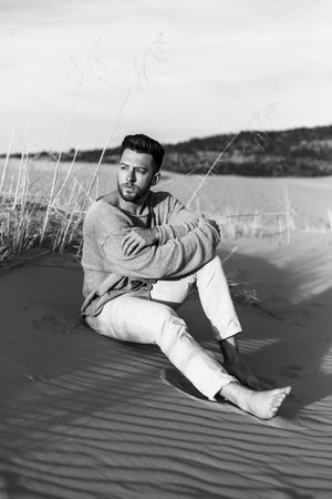 Black and white photo series of a person in a sweater reclining on sand dunes against a scenic backdrop.