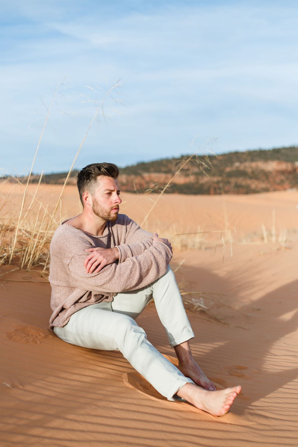 Figure relaxing on sand dunes wearing casual attire against a blue sky backdrop.